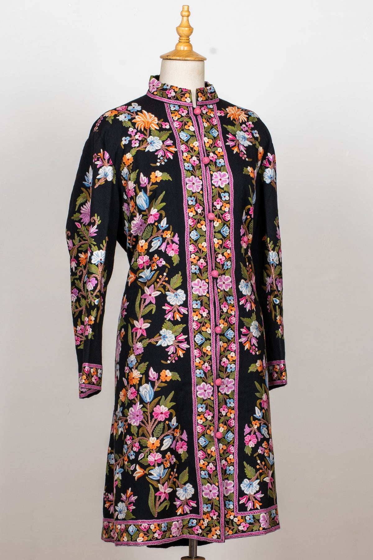 Full front view of the black long jacket with colourful floral vines, a stand collar and pink-edged cuffs and hem