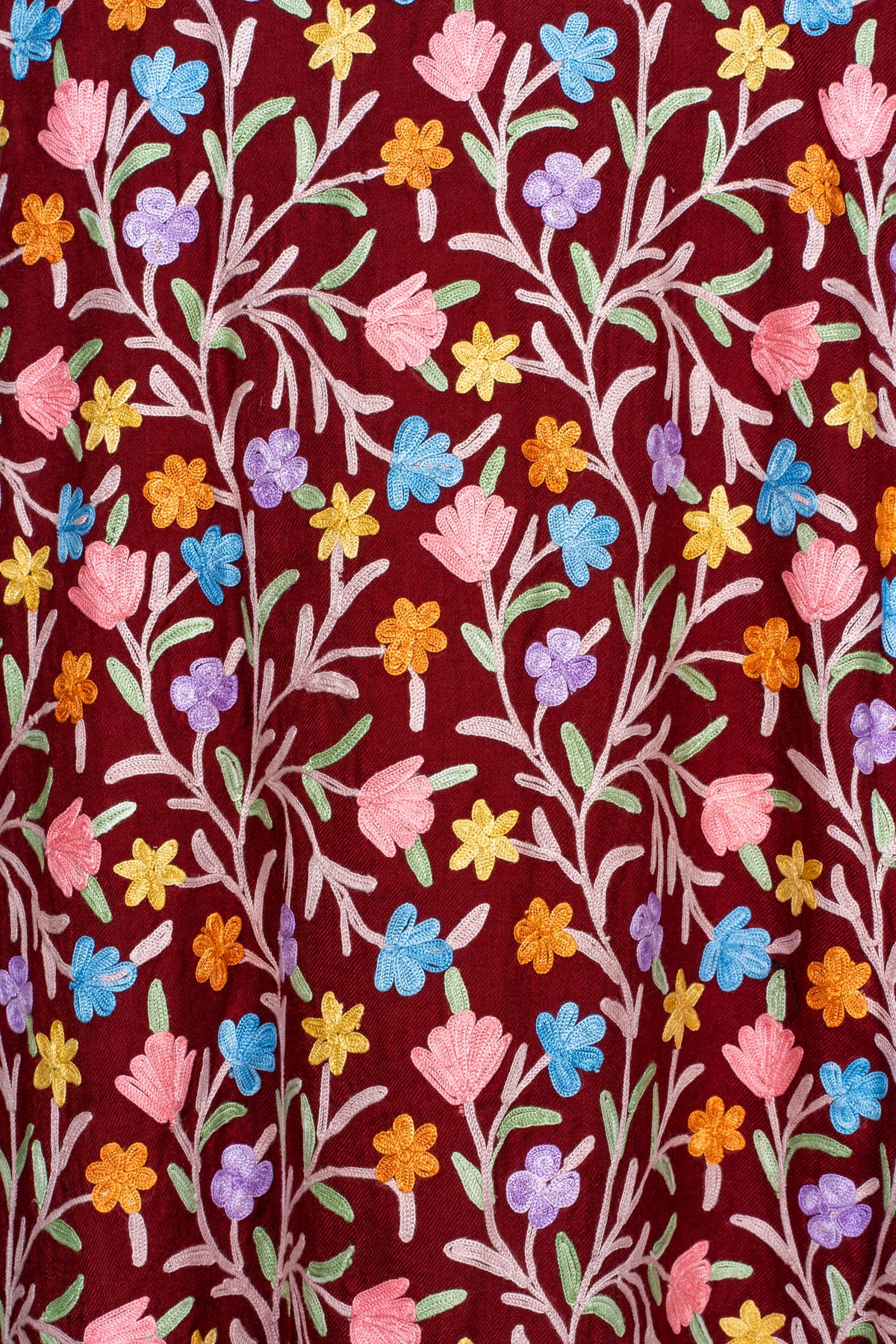 Close-up of the maroon fabric with vertical pale vines, green leaves and small multicoloured embroidered flowers.