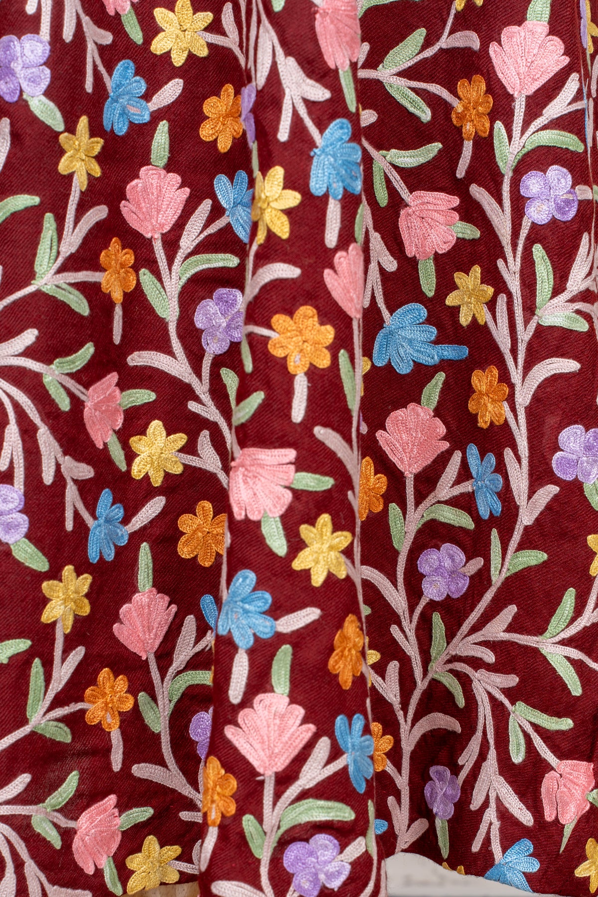 Close-up of hanging maroon abaya folds with colourful Aari flowers and pale leafy stems.