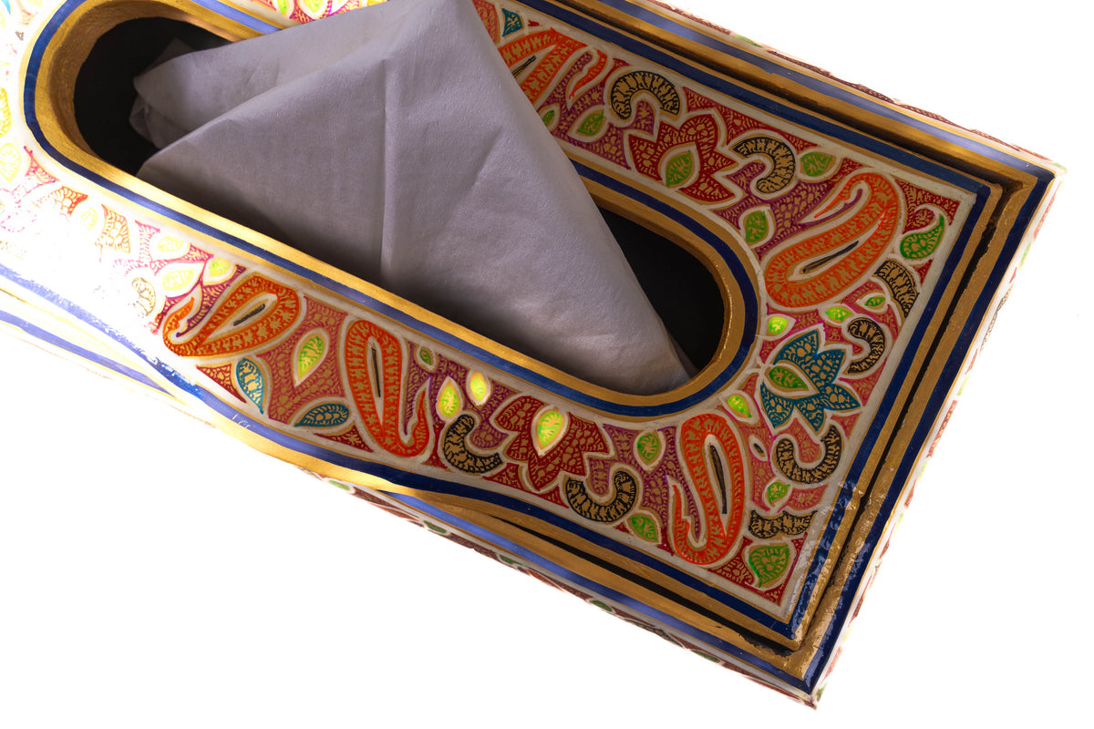 Close-up of the tissue box’s oval opening and painted orange-and-green paisleys, with a tissue rising from the slot