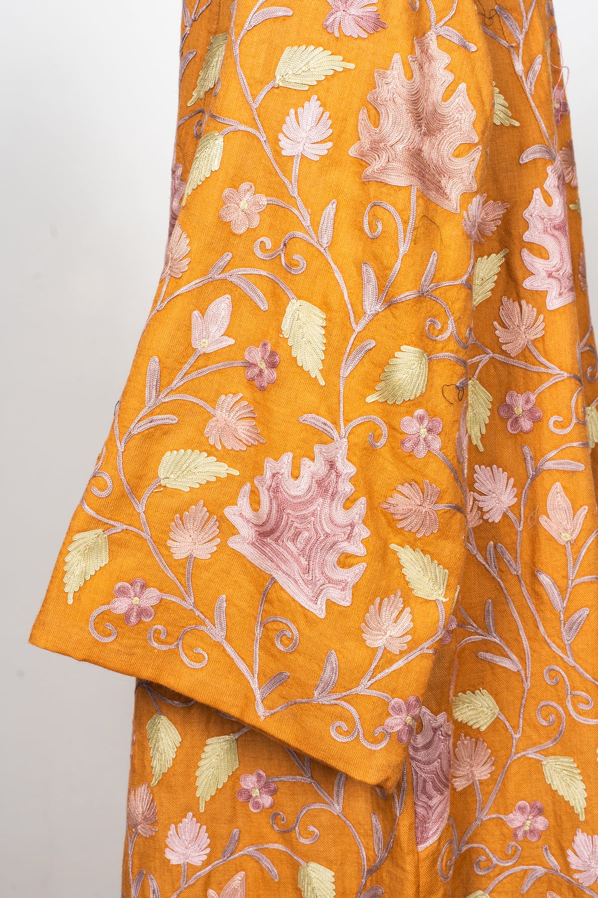 Close-up of an amber sleeve and cuff embroidered with lilac Aari leaves, pale green foliage and curling stems