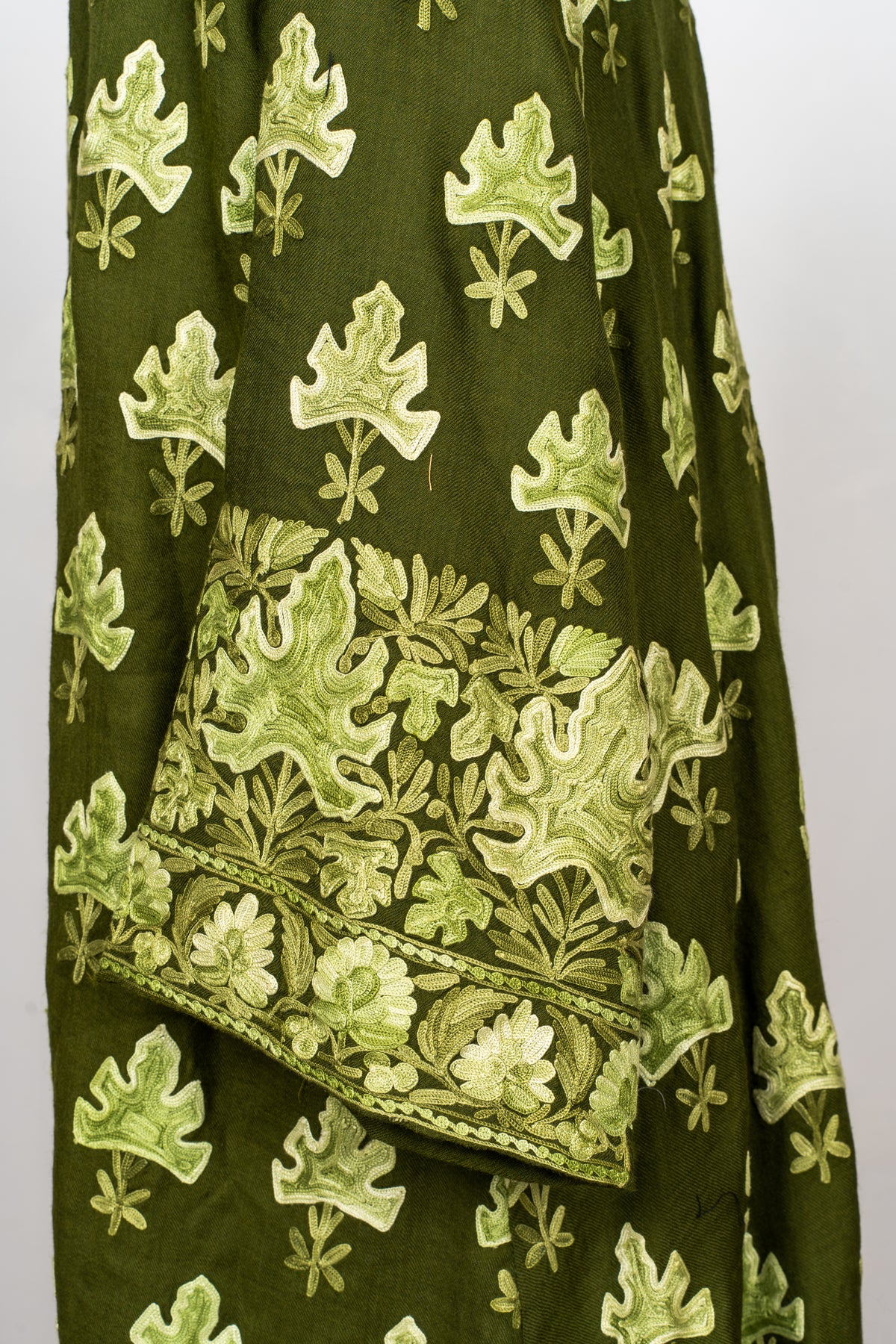 Cuff detail of the olive abaya with dense pale green leaves and a floral border beneath scattered leaf motifs.