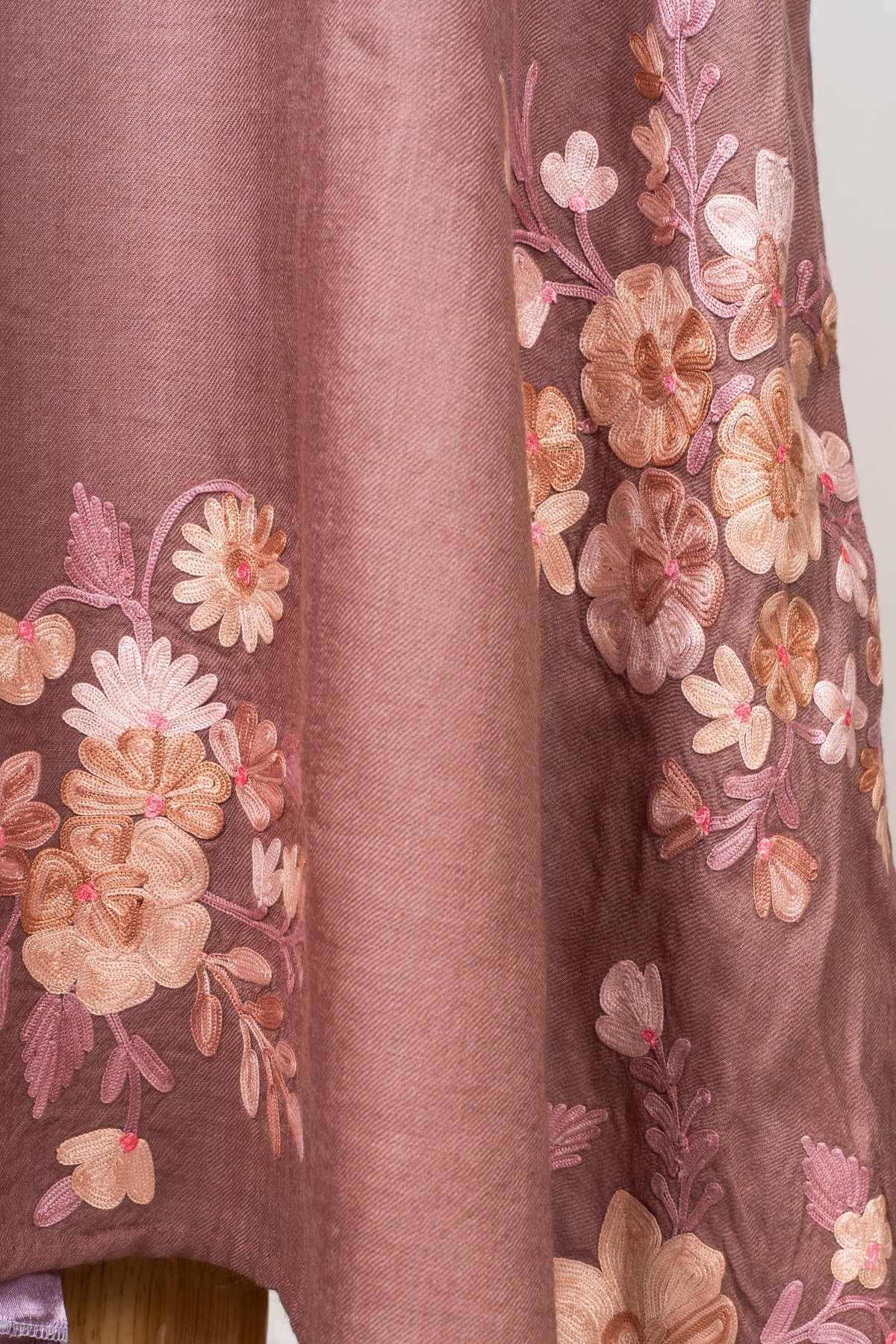 Close-up of pale pink, peach and ivory Aari flower bouquets across hanging folds of a dusty rose abaya