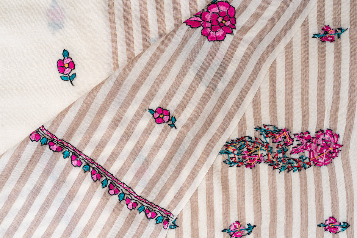 Folded corner of the striped ivory shawl showing pink floral edging and the reverse stitching of a larger motif