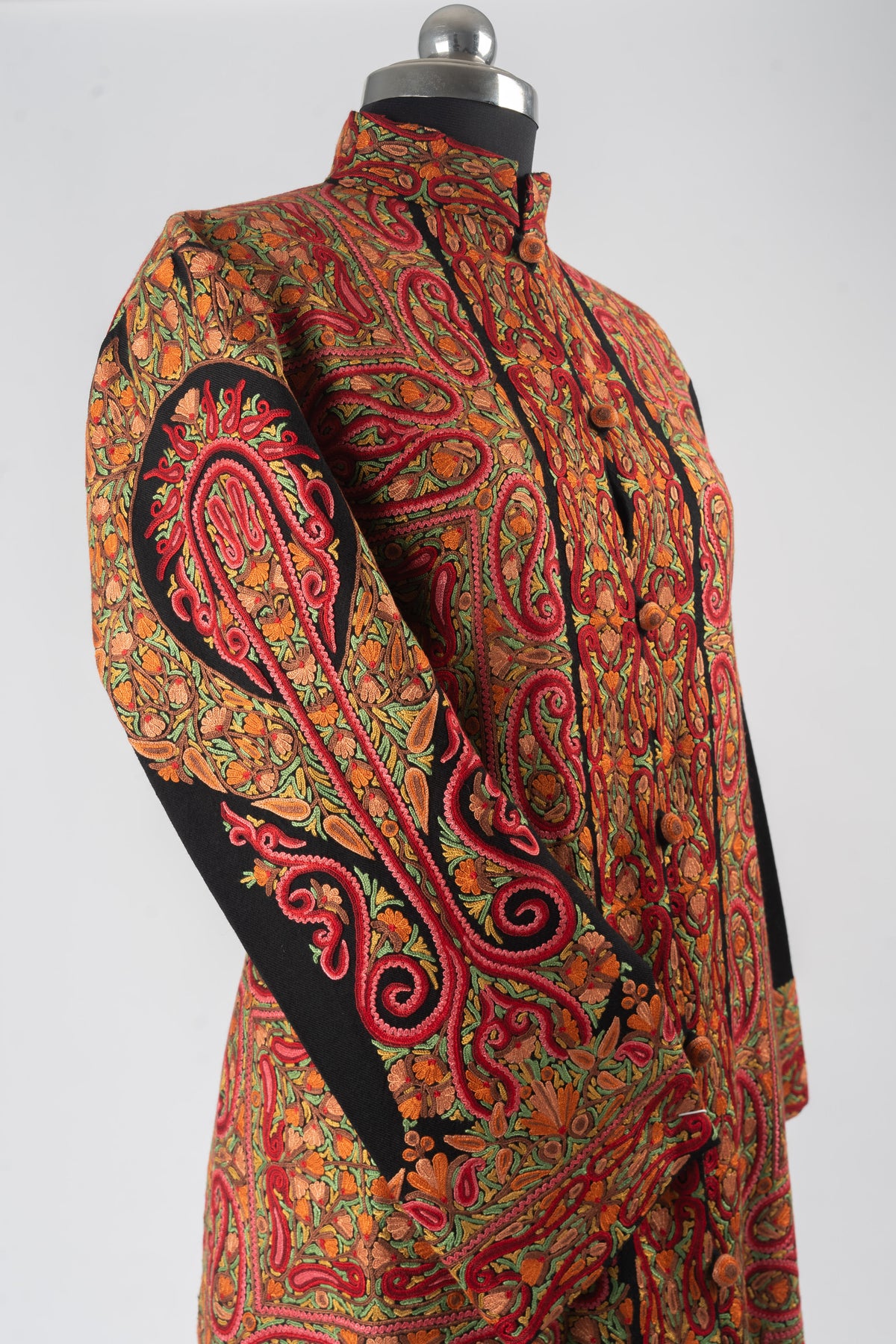 Angled upper view of a black jacket with a large red and orange Aari sleeve motif and dense paisley panels on the front