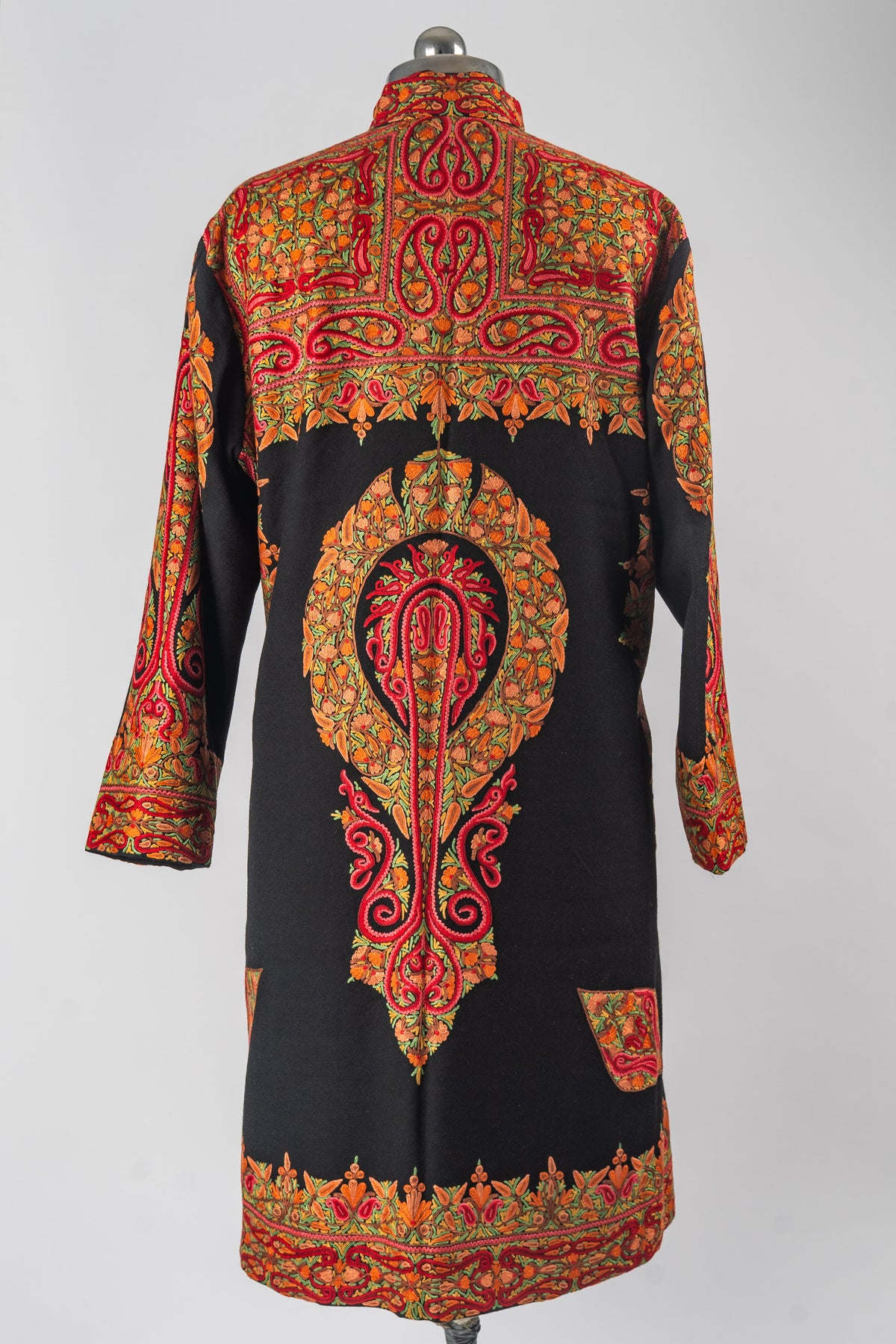 Back of a black Merino wool jacket with an elongated red and orange Aari floral medallion and embroidered shoulder and hem panels