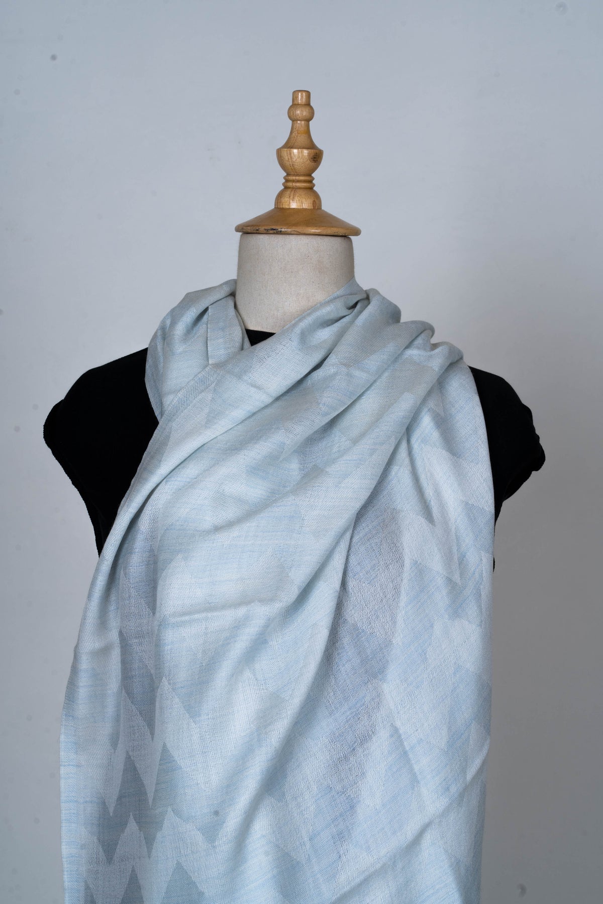 Pale blue stole wrapped broadly across a mannequin’s chest, showing subtle tonal geometric shapes in the weave.