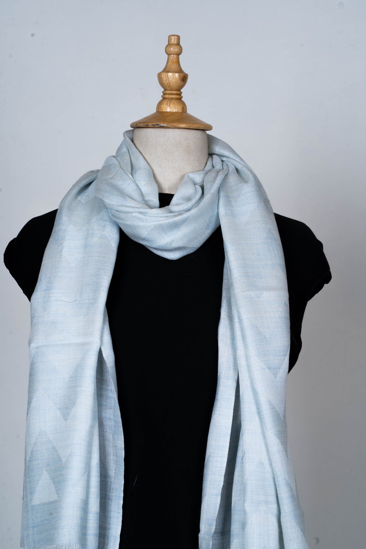 Upper view of the pale blue merino wool stole loosely looped at the neck, with both ends hanging over a black top.