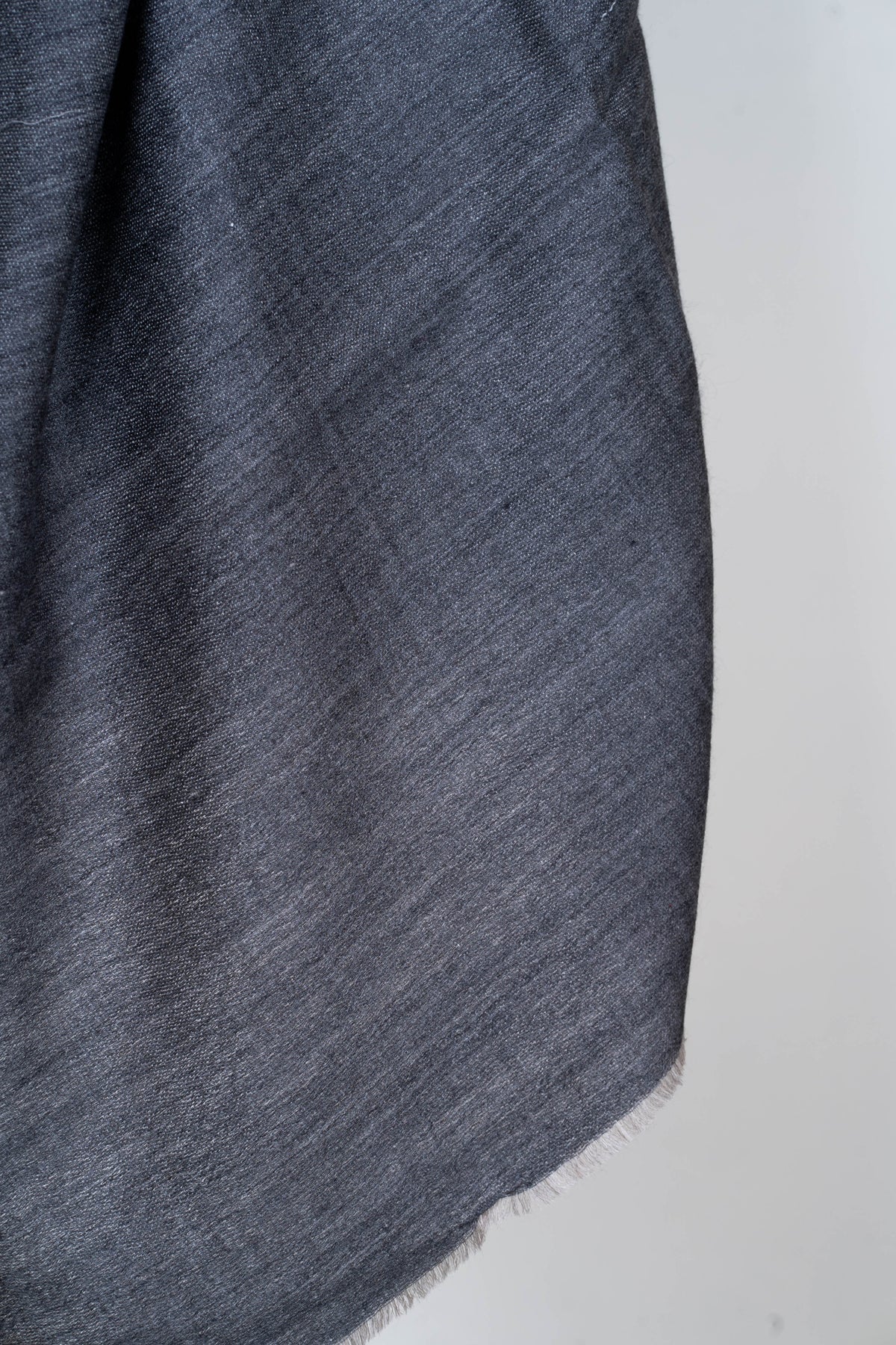 Close-up of the plain charcoal-grey weave and short softly fringed edge of a Merino wool stole