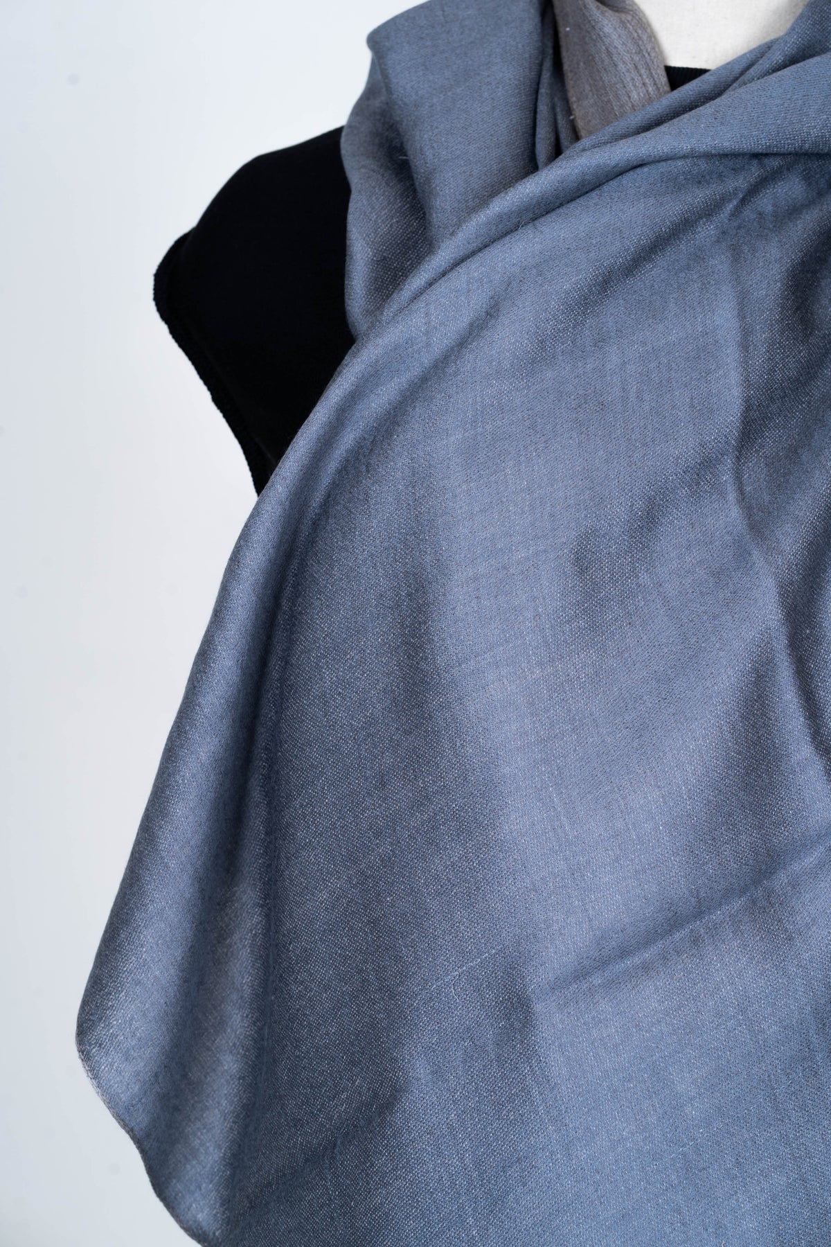 Close-up of the steel blue side of a reversible Merino wool stole, draped in soft folds over a mannequin