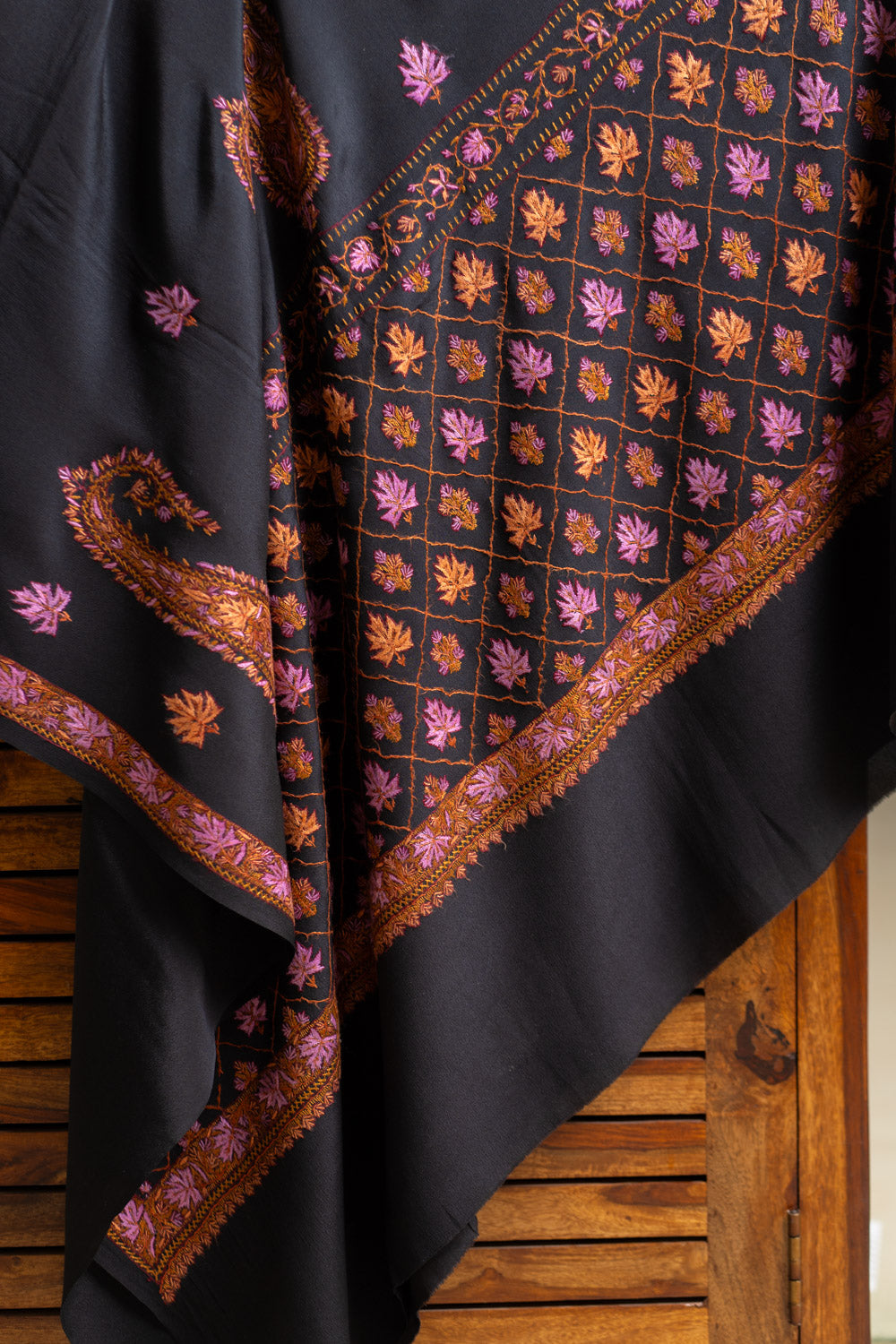 Angled drape of a black crepe saree showing its orange and pink Sozni lattice pallu and narrow leaf border