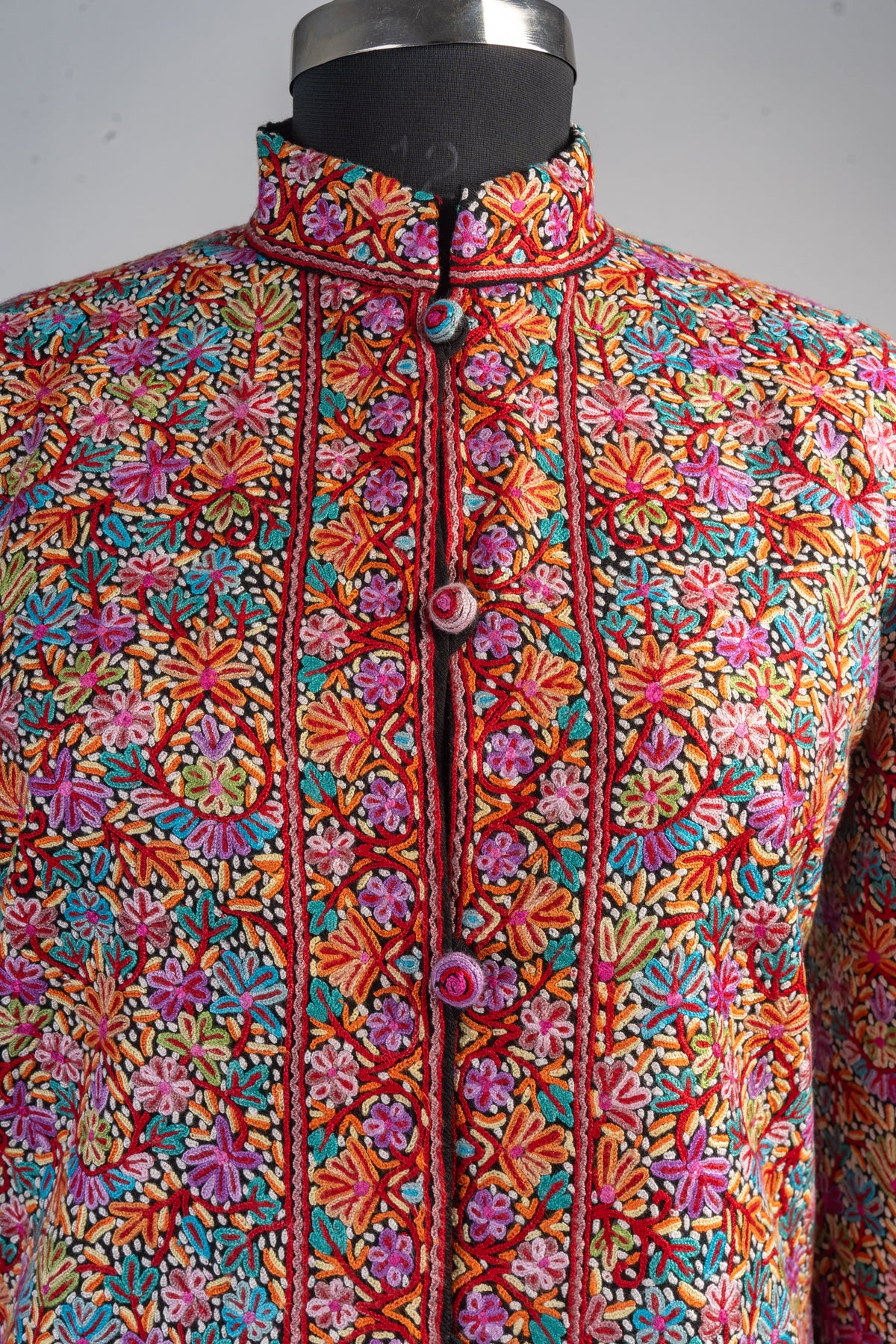 Upper front of the embroidered merino wool jacket, with a floral stand collar, patterned opening borders and round covered buttons.
