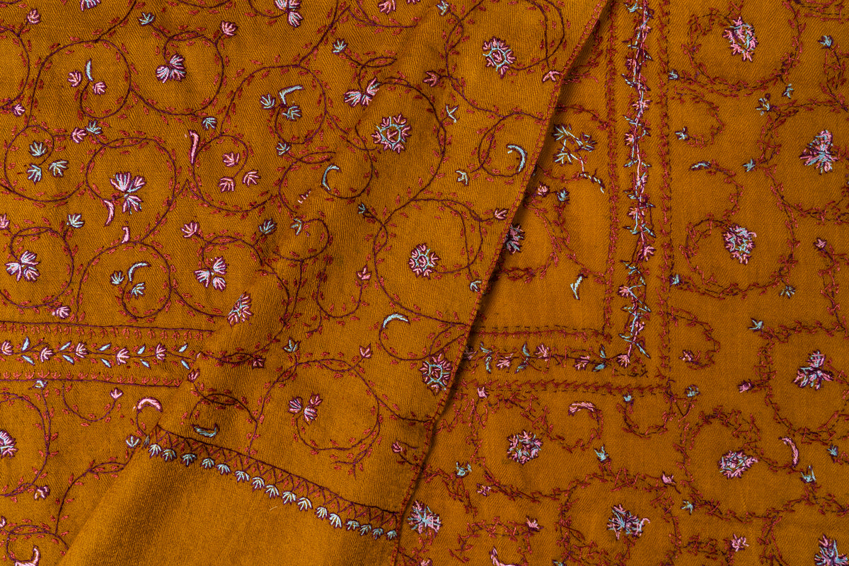 Folded mustard stole corner revealing both sides of fine Sozni floral vines and pink and white border stitching