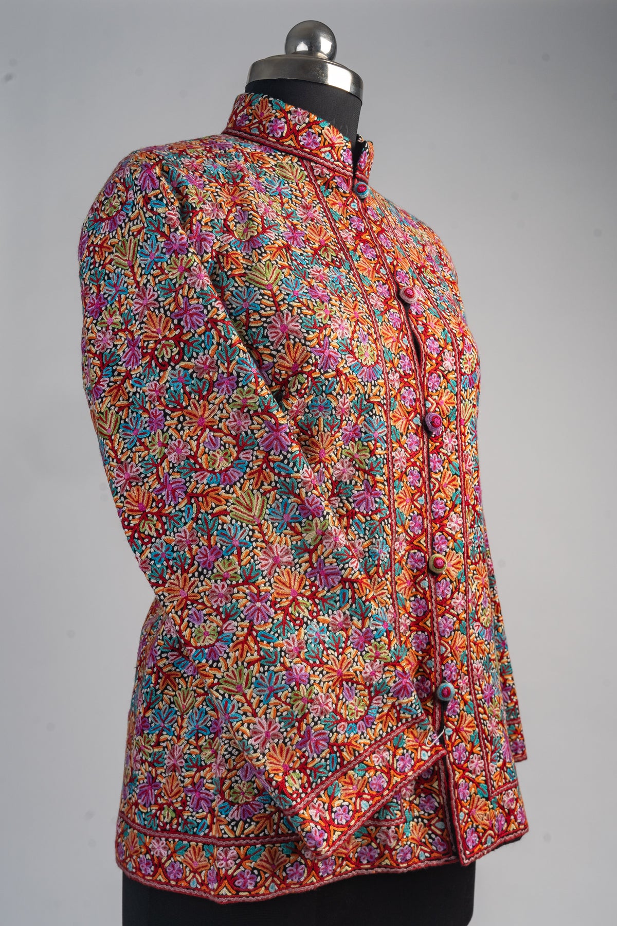 Angled front of the short floral Aari jacket on a mannequin, showing the stand collar, covered buttons and one sleeve crossed.