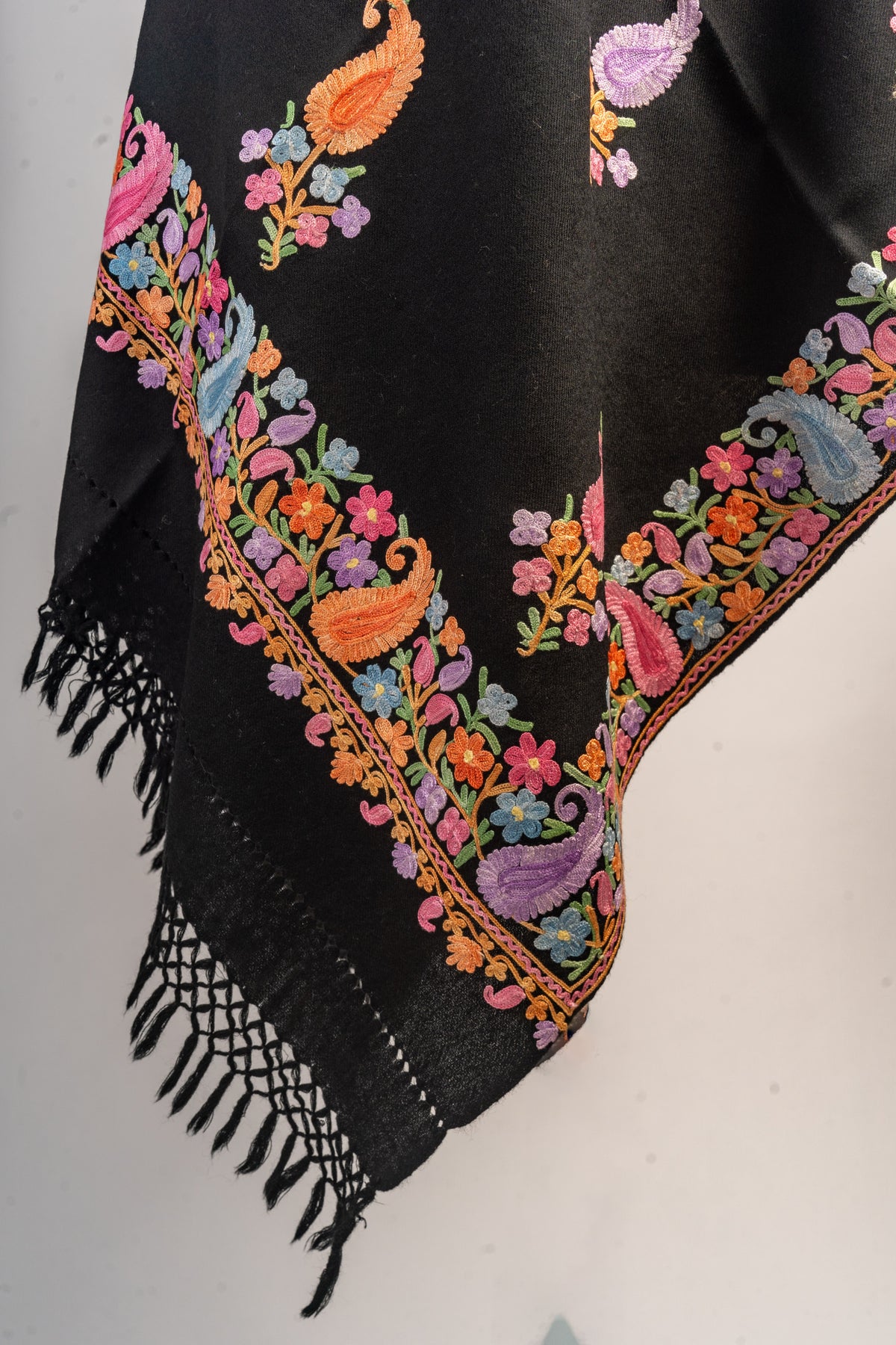 Hanging corner of the black stole with a colourful embroidered paisley border, scattered motifs and knotted fringe.