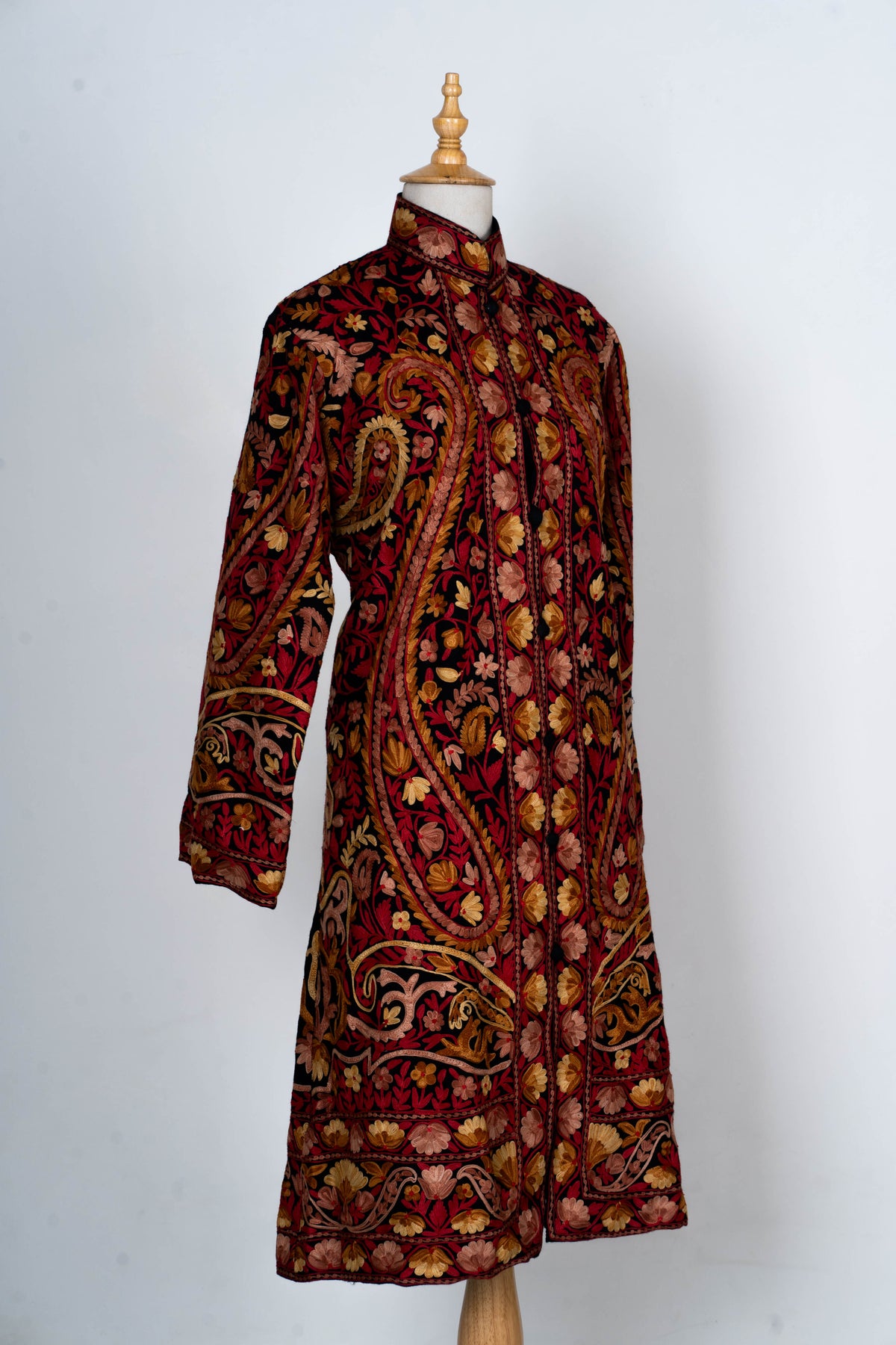 Full angled view of the embroidered long jacket, showing its fitted shape, front fastening and patterned hem and cuffs.