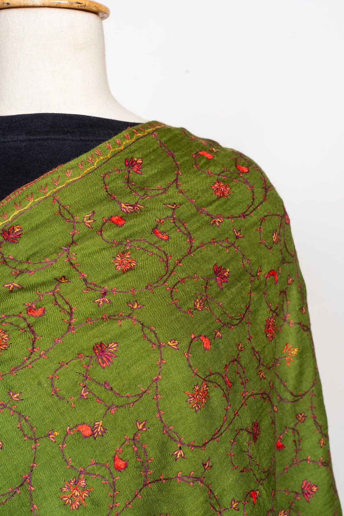 Close-up of an olive-green stole over a mannequin's shoulder with fine maroon vines and scattered red and pink flowers