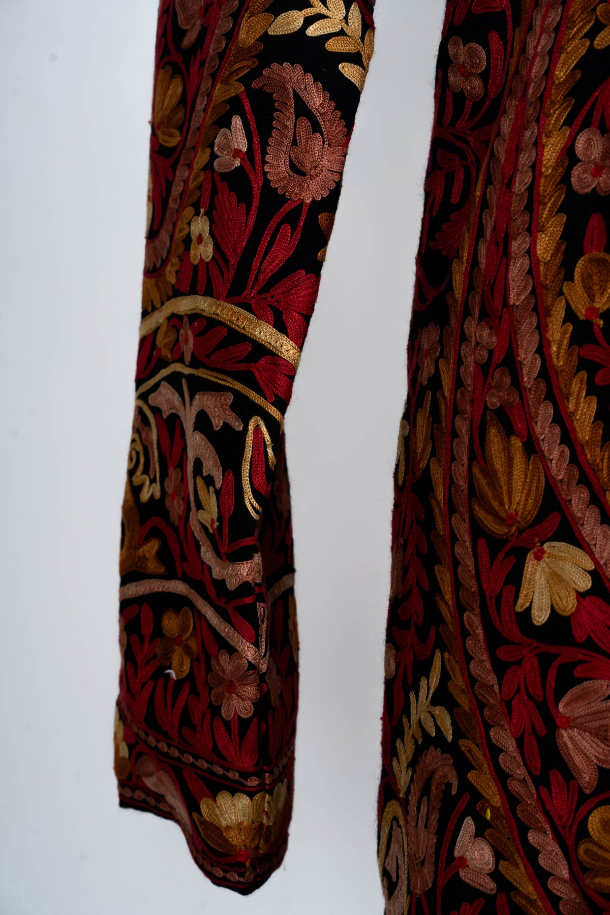 Close-up of the jacket sleeve and cuff with red stems, gold and blush flowers, and curved embroidered bands.