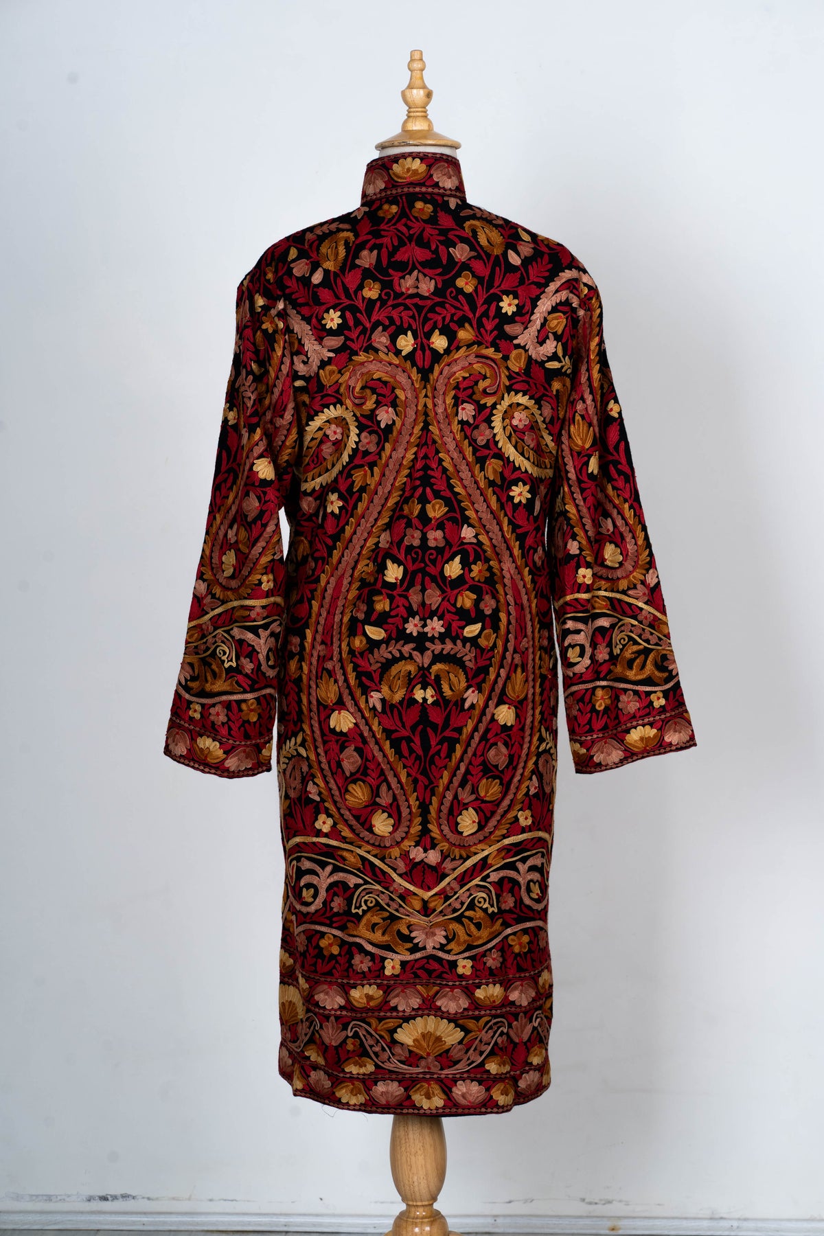 Full back view of the long black jacket, with large mirrored paisleys, dense floral embroidery and patterned hem borders.