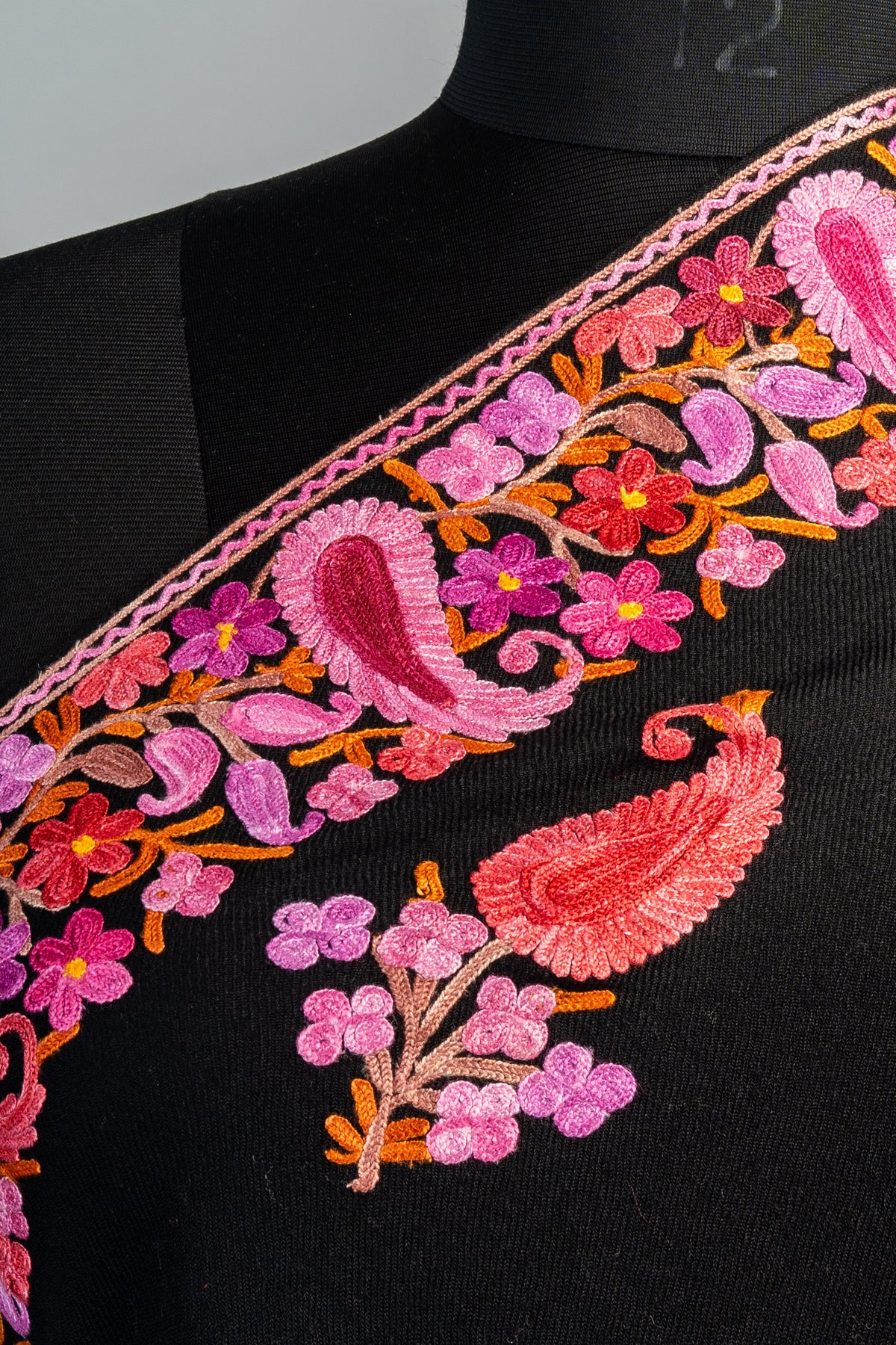 Shoulder close-up of the black stole’s pink paisley and flower border beside a coral-pink paisley sprig