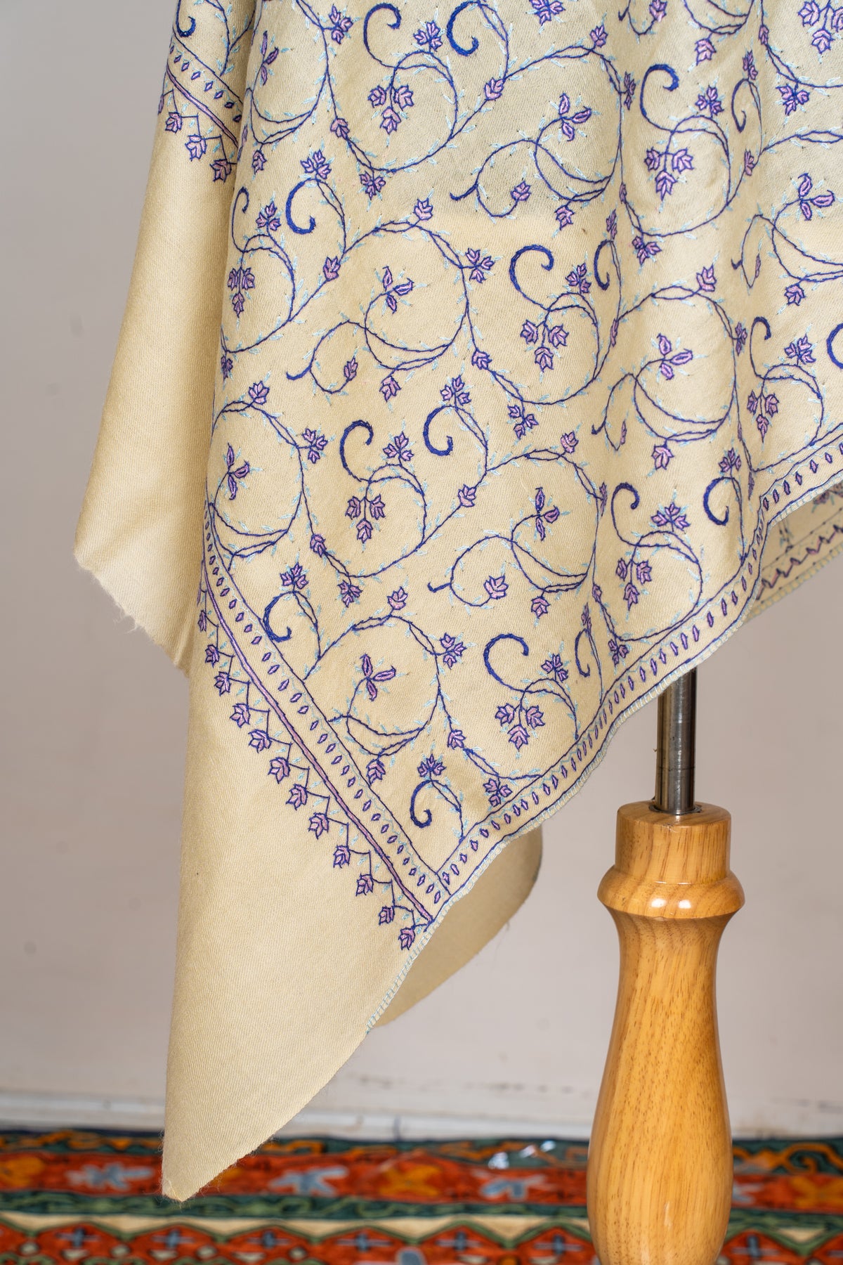 Hanging corner of a cream stole with curling purple floral embroidery, a narrow patterned border and a plain end