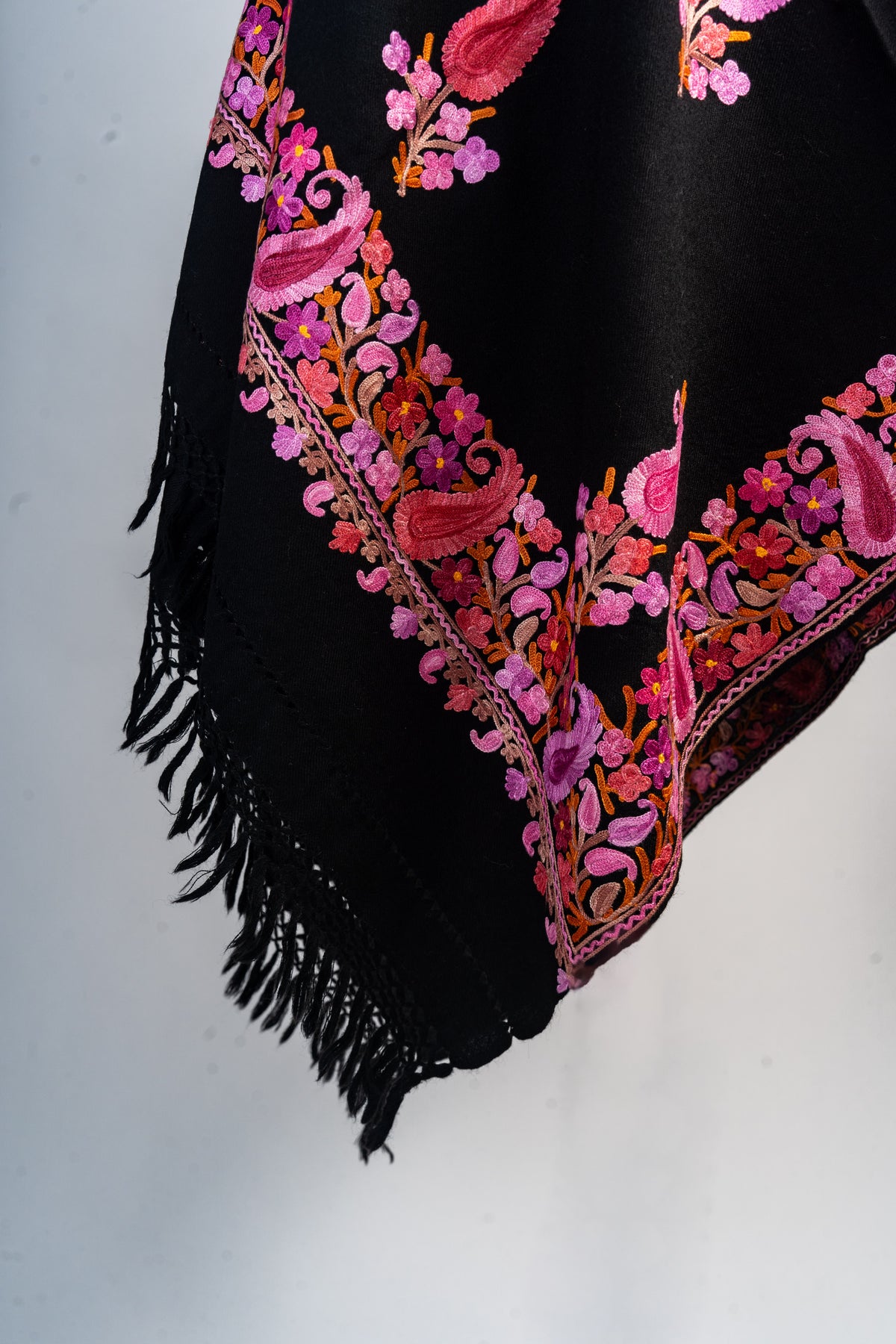 Hanging black stole corner with pink paisleys, purple flowers and orange stems above knotted black fringe