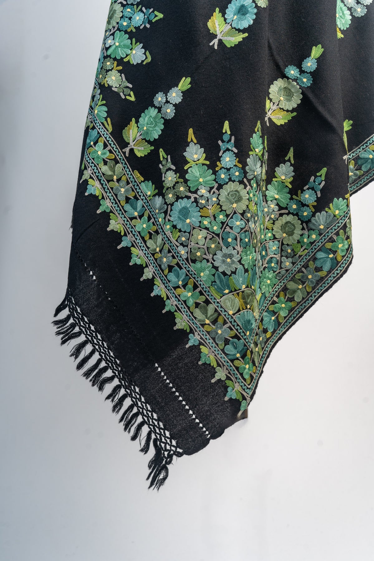 Hanging corner of the black stole with dense mint and green floral embroidery, patterned borders and black fringe.