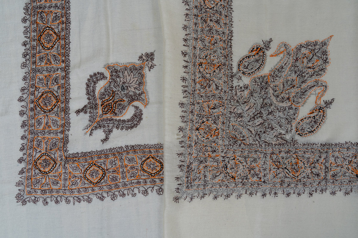 Overlapping corners of an ivory rumal, showing both sides of the charcoal and ochre Sozni border and paisley embroidery