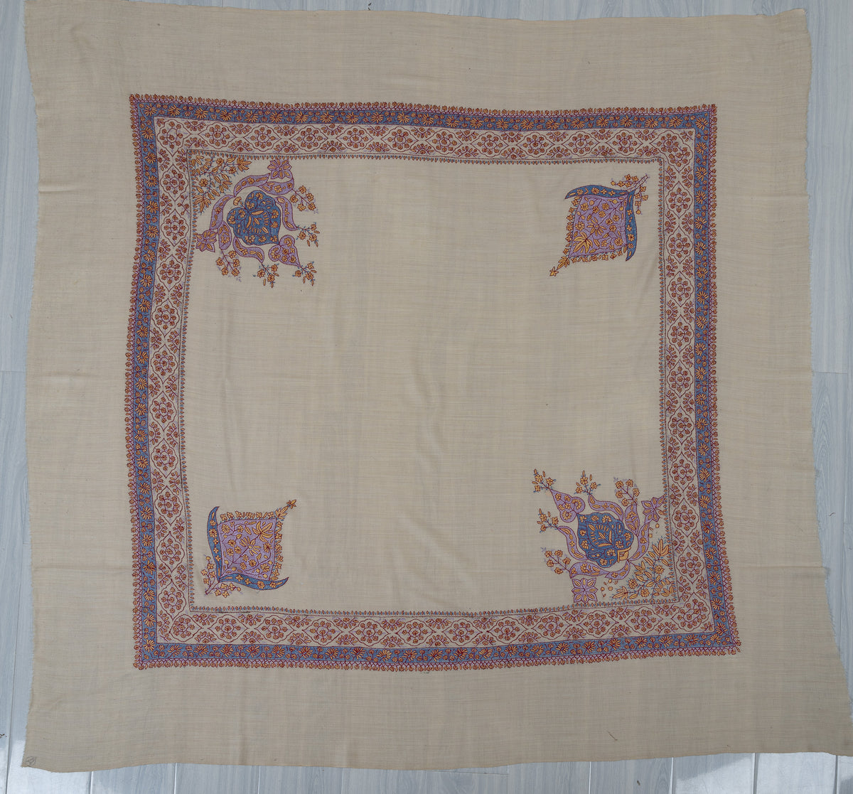 Pearl-coloured square Merino wool rumal laid flat, with blue and coral floral borders and four blue and lavender corner motifs