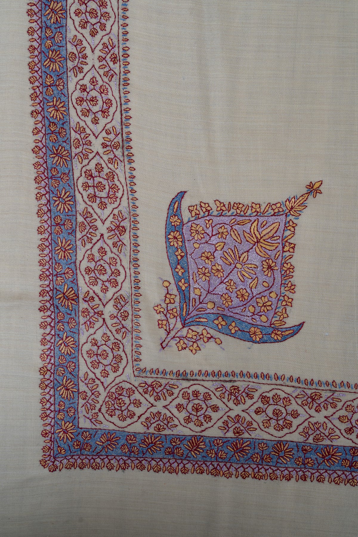 Corner of a pearl-coloured rumal with a lavender leaf-shaped floral motif beside a blue and coral Sozni border