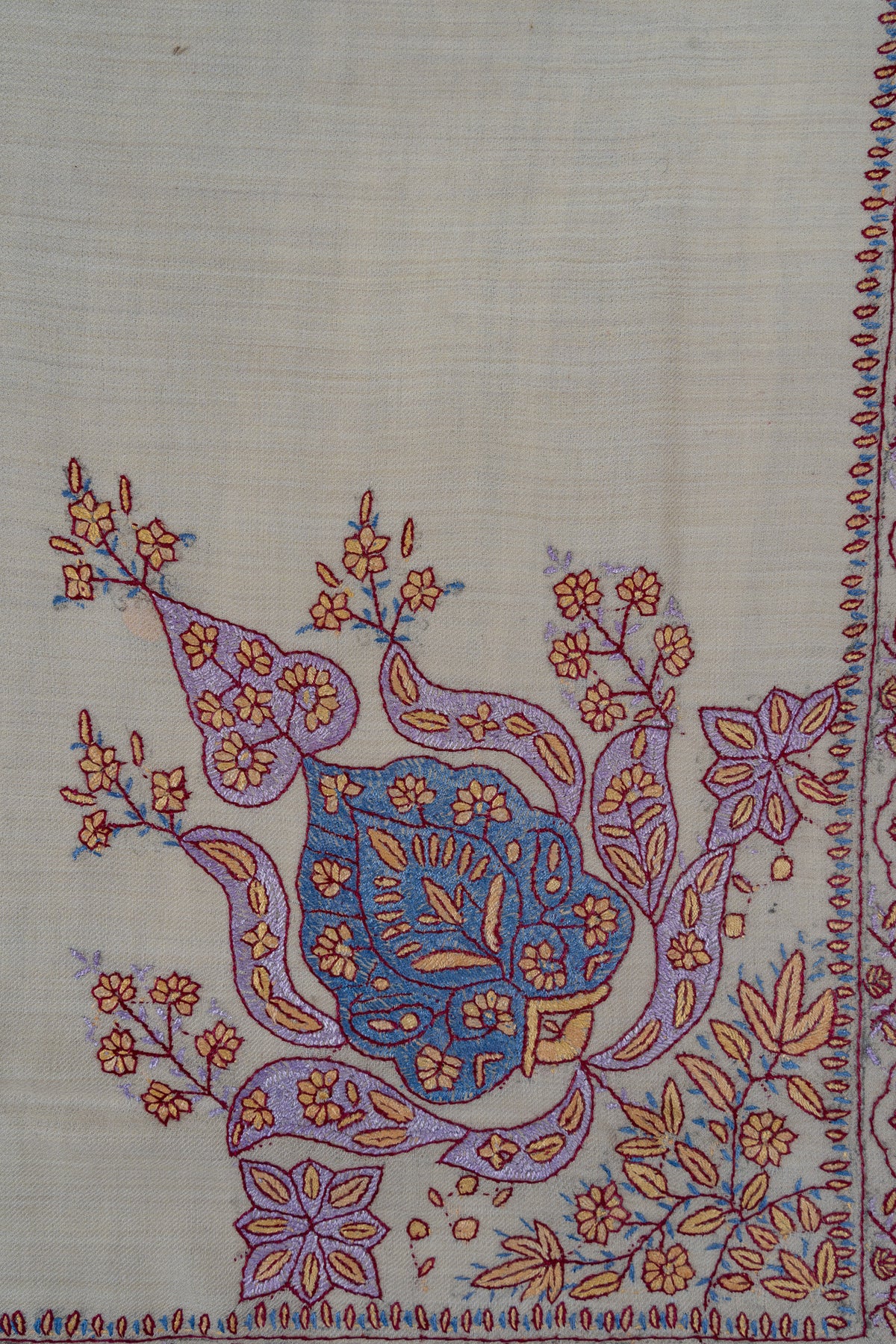 Close-up of blue and lavender curling paisleys with coral-outlined flowers in the corner of a pearl-coloured rumal