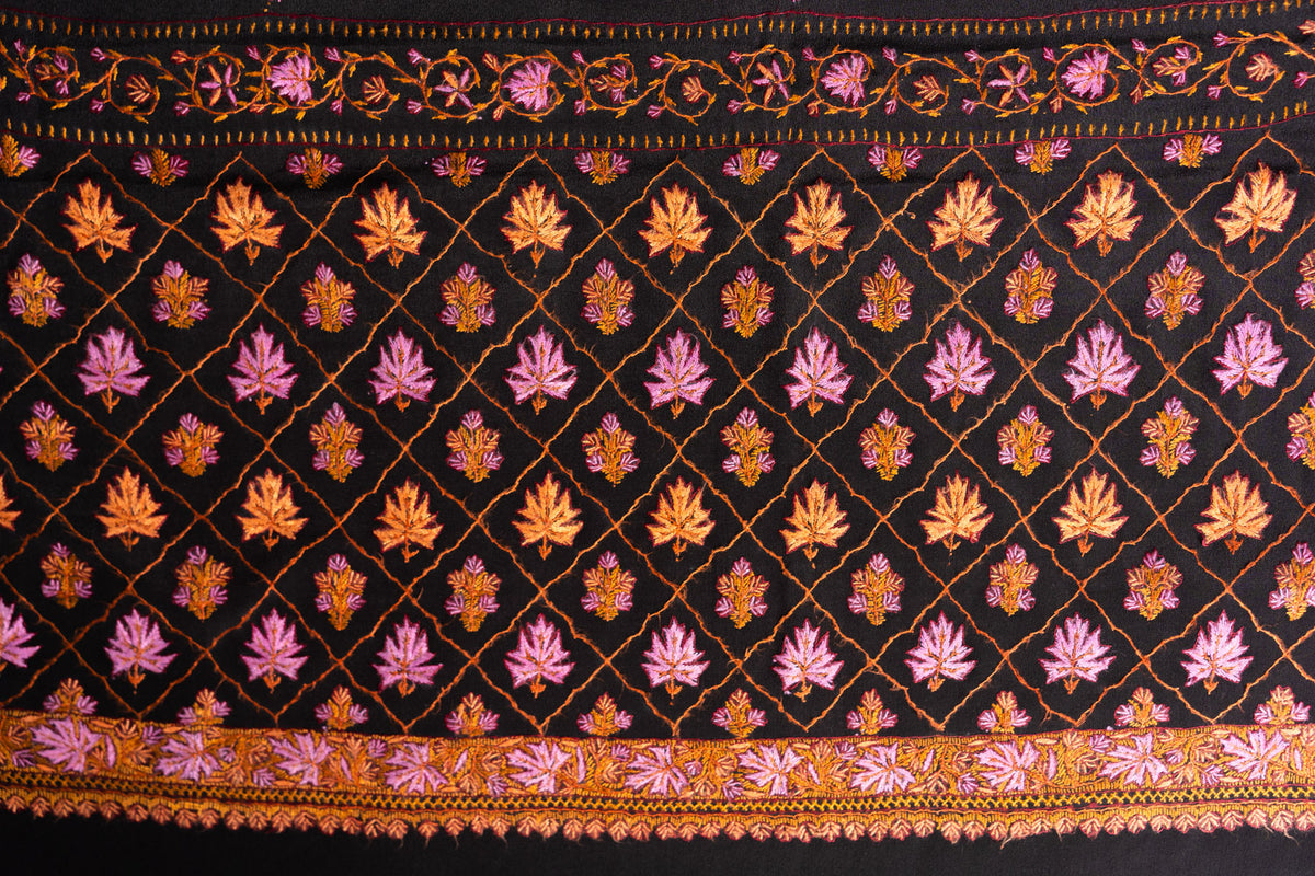 Close-up of the black saree pallu with pink and orange Sozni leaf motifs inside a diamond lattice and floral edge borders