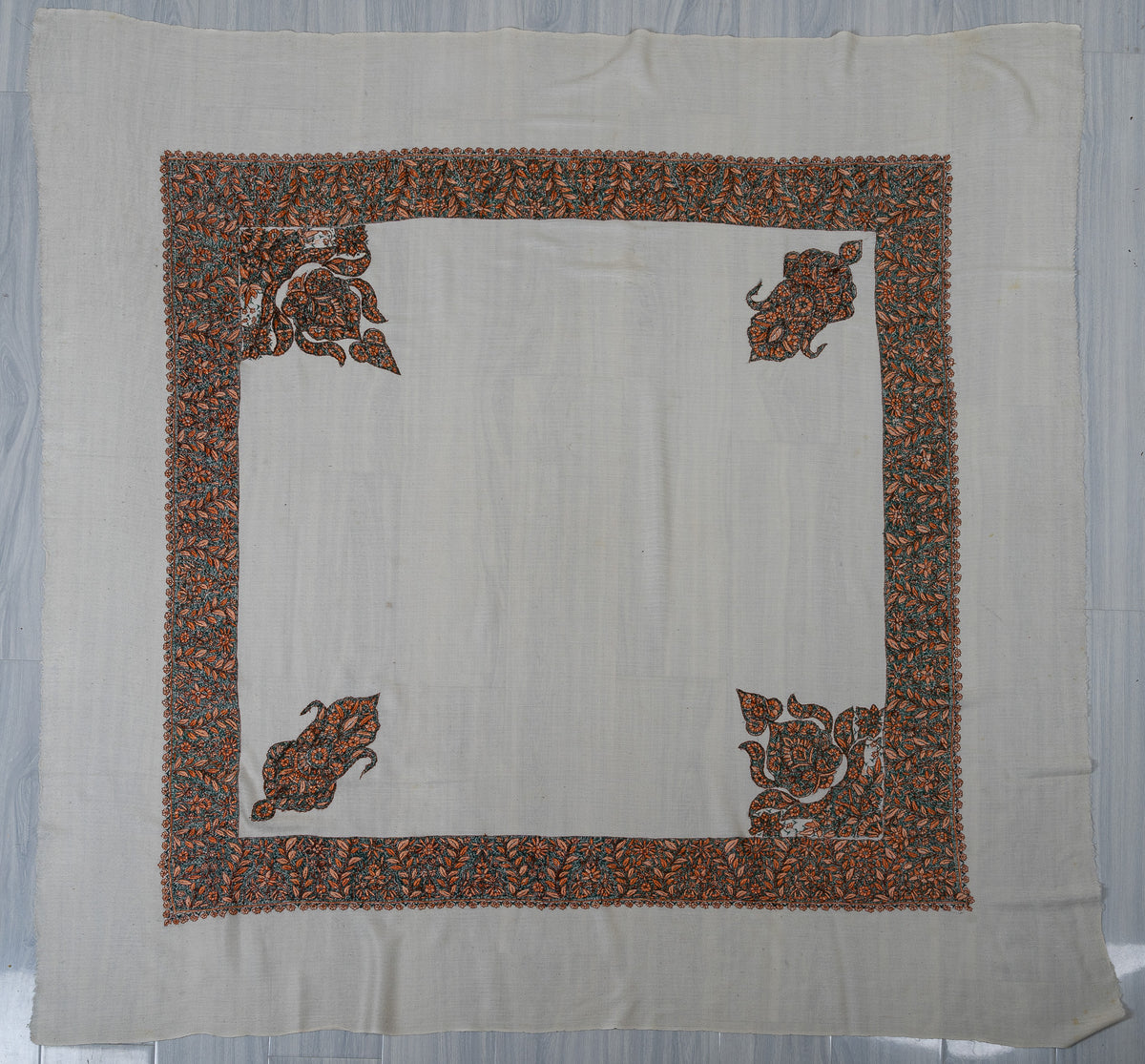 Ivory rumal laid flat with dense teal and orange floral borders and alternating large and small corner motifs
