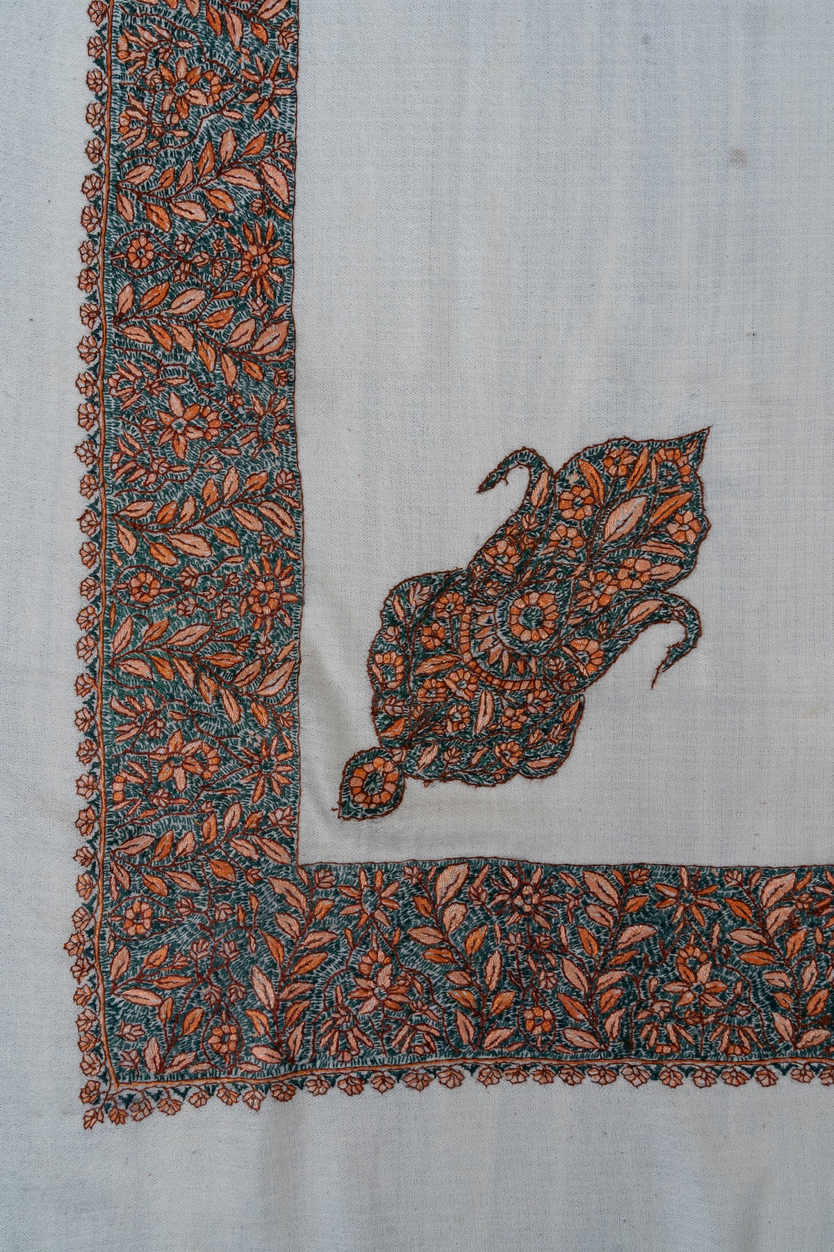 Corner detail of an ivory rumal with a teal and orange Sozni motif inside a broad floral border