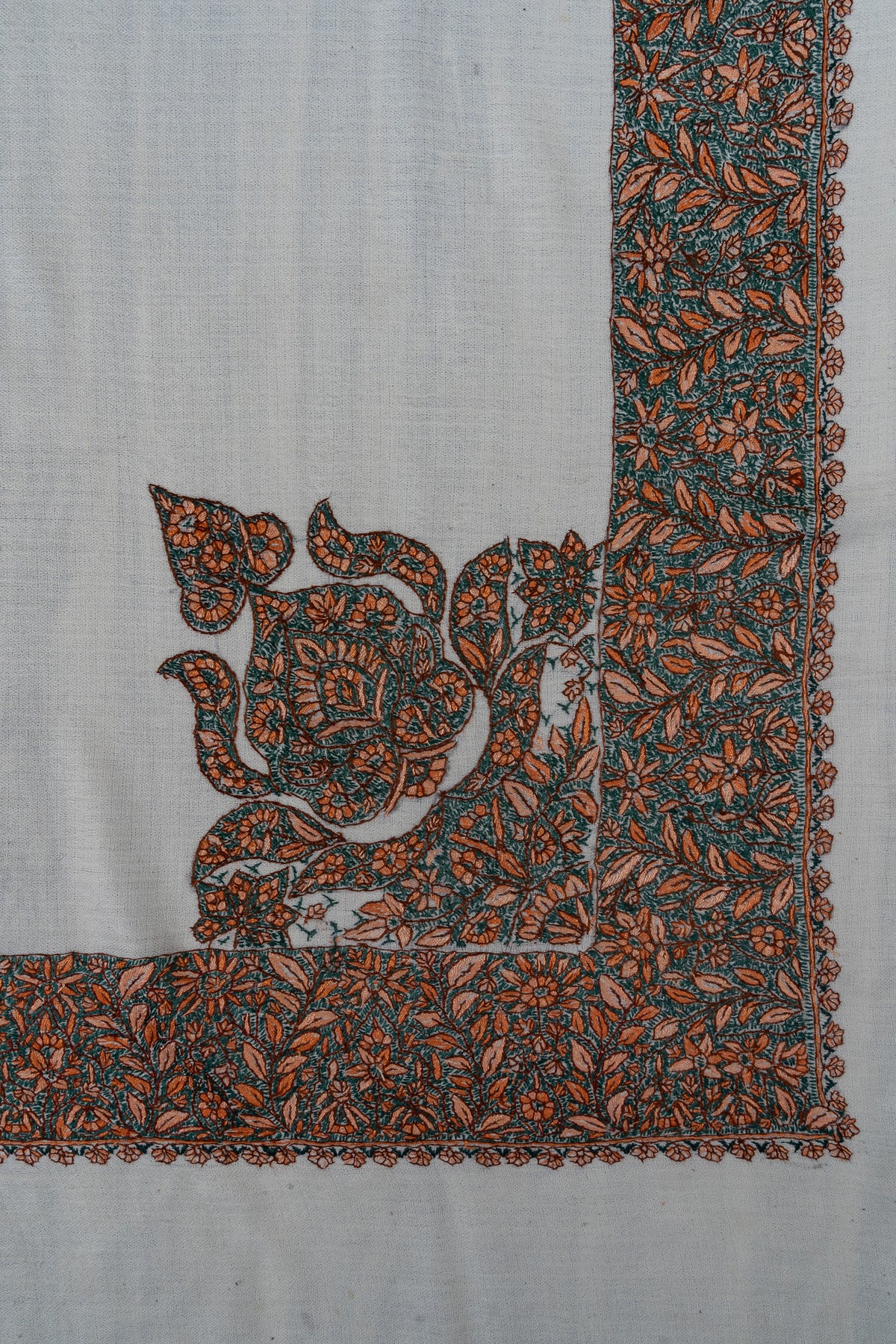 Corner of an ivory rumal showing a large teal and orange Sozni floral panel joined to a dense matching border