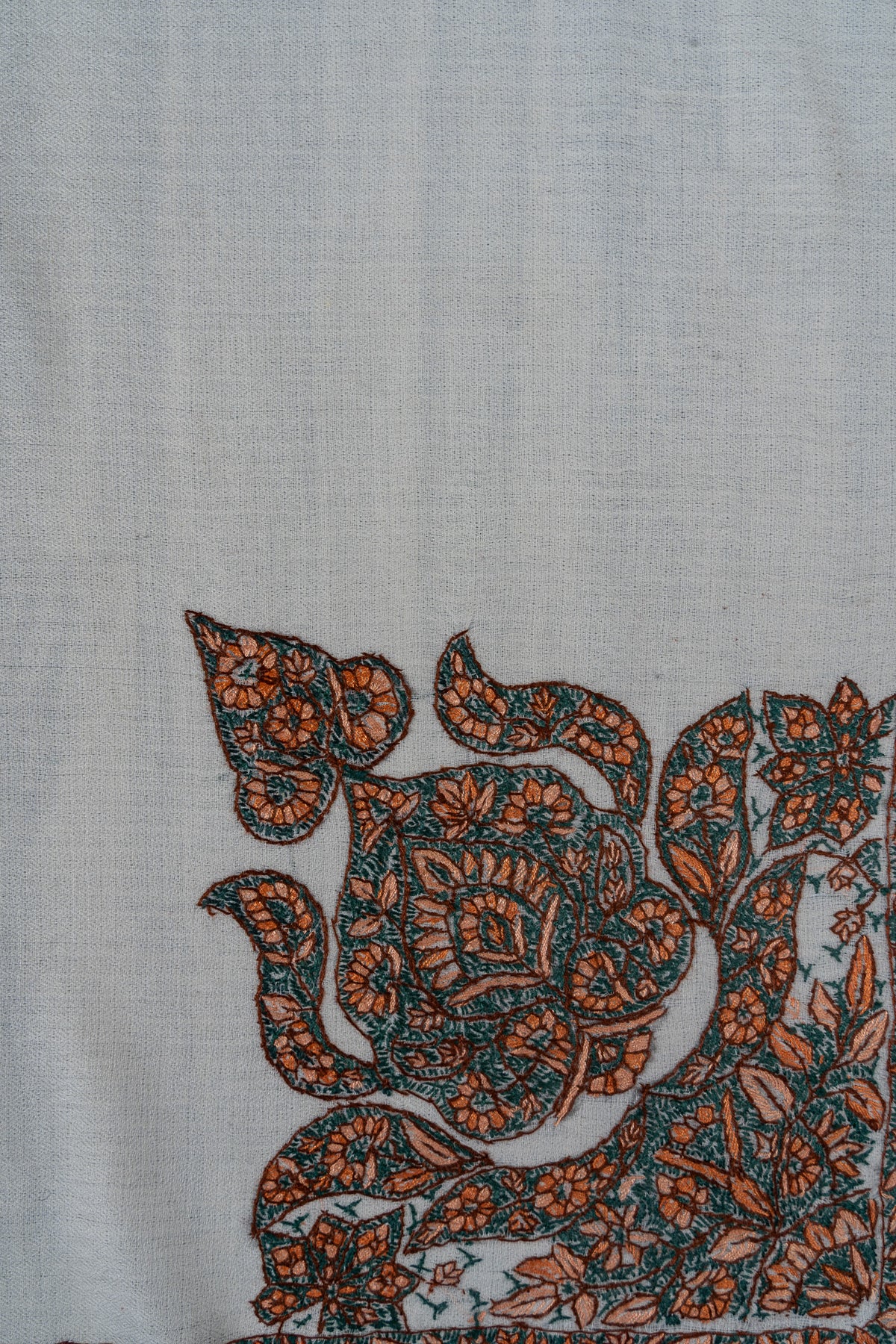 Close-up of teal and orange Sozni flowers and curved leaves in a large ivory rumal corner panel