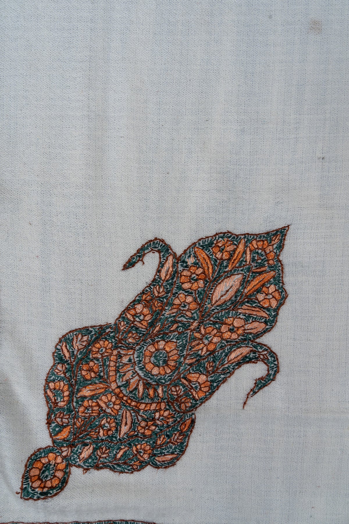 Close-up of an ornate teal and orange Sozni motif filled with flowers and leaves on ivory Merino wool