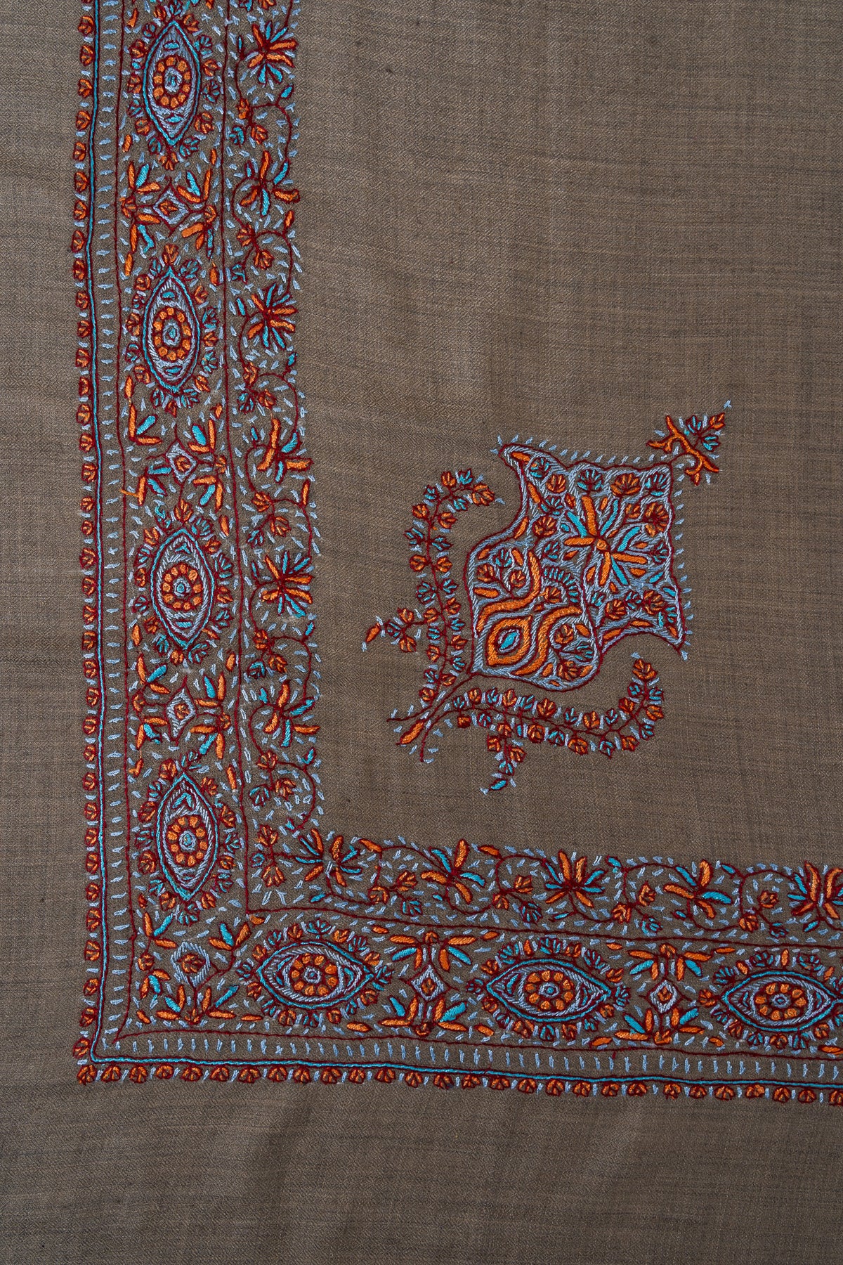 Corner of a cedar-brown rumal with a small turquoise and copper floral motif beside an ornate Sozni border