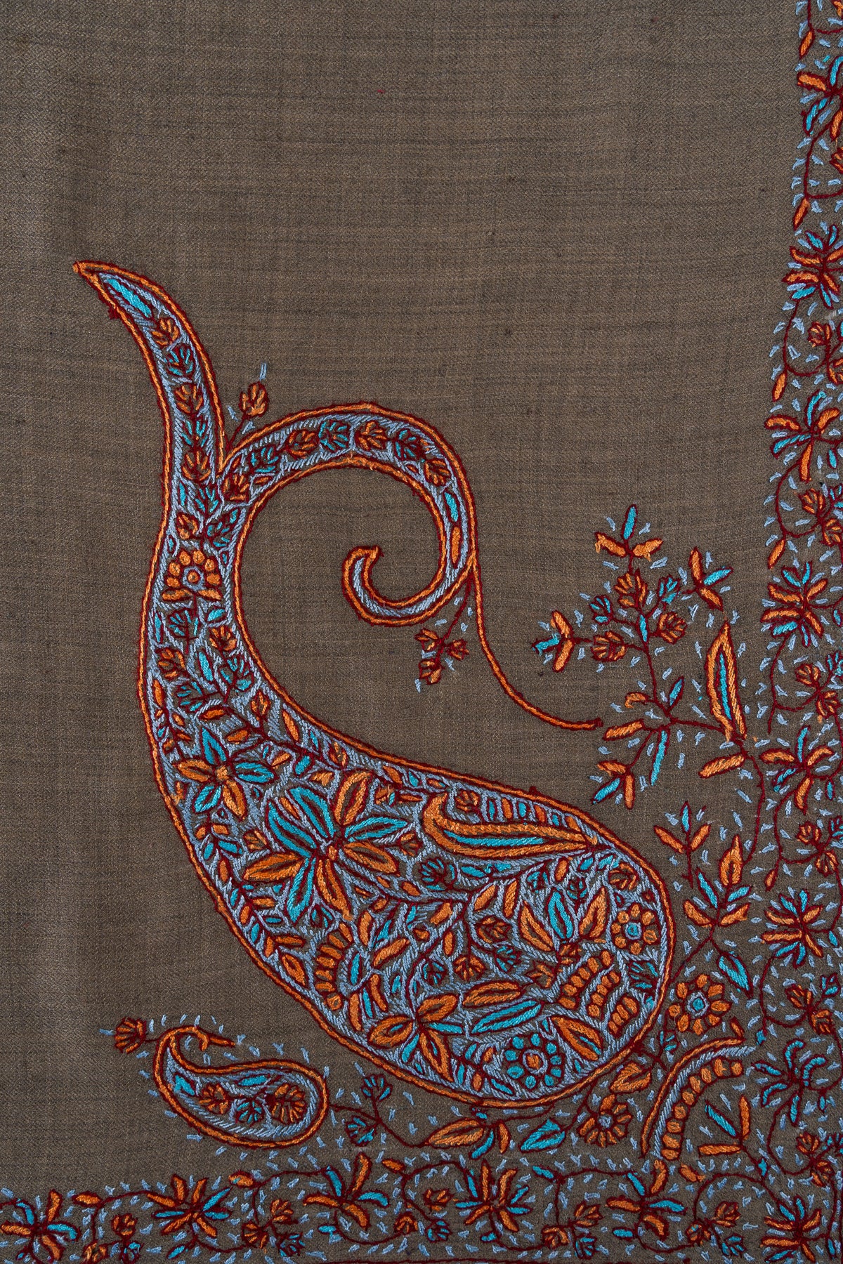 Close-up of a long curling Sozni paisley filled with turquoise and copper flowers on cedar-brown rumal fabric