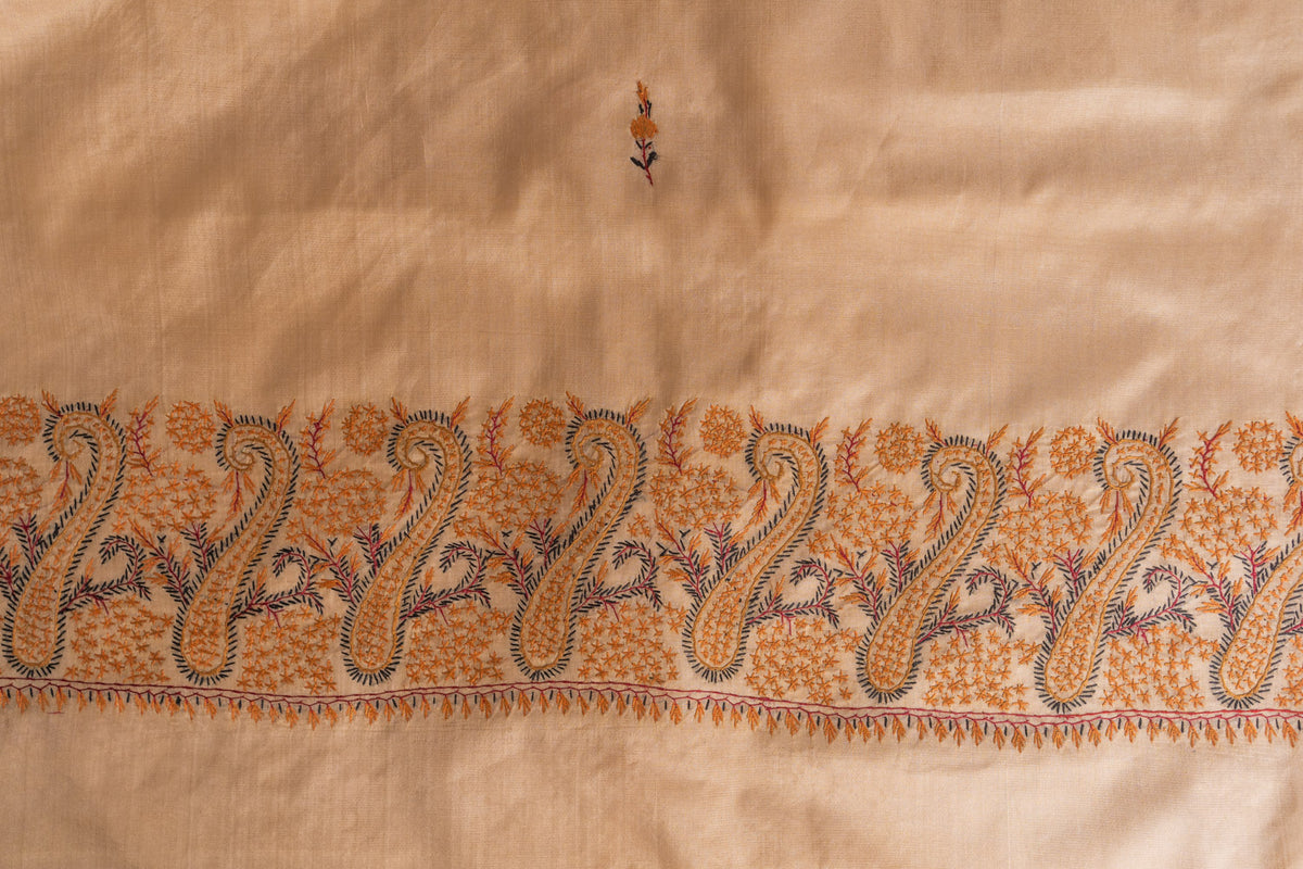Flat view of the ivory silk saree’s orange-and-blue Sozni paisley band with a small embroidered sprig above.