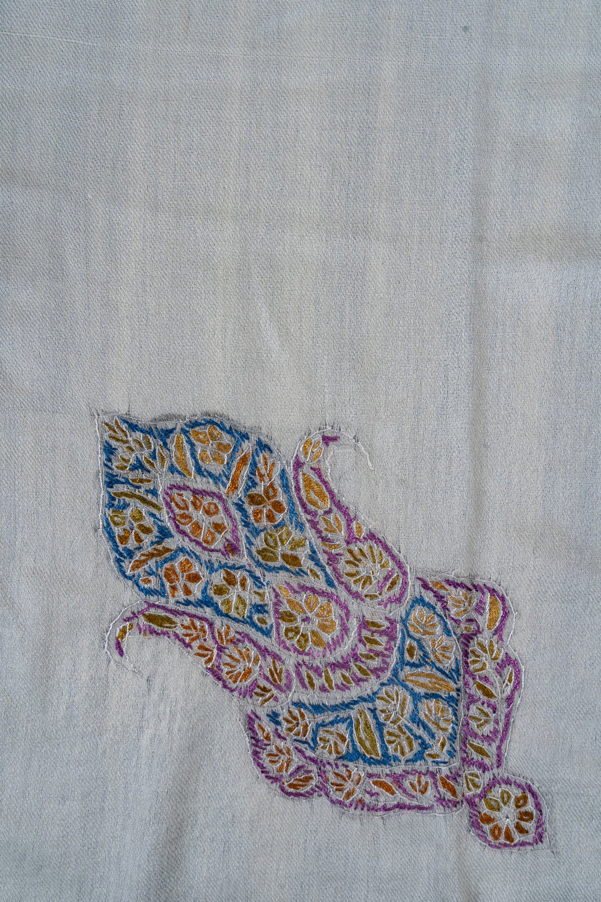 Close-up of an elongated purple, blue and gold Sozni floral motif on ivory rumal fabric