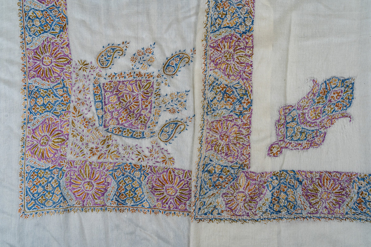 Overlapping ivory rumal corners, showing the purple, blue and gold floral border and two different embroidered corner motifs