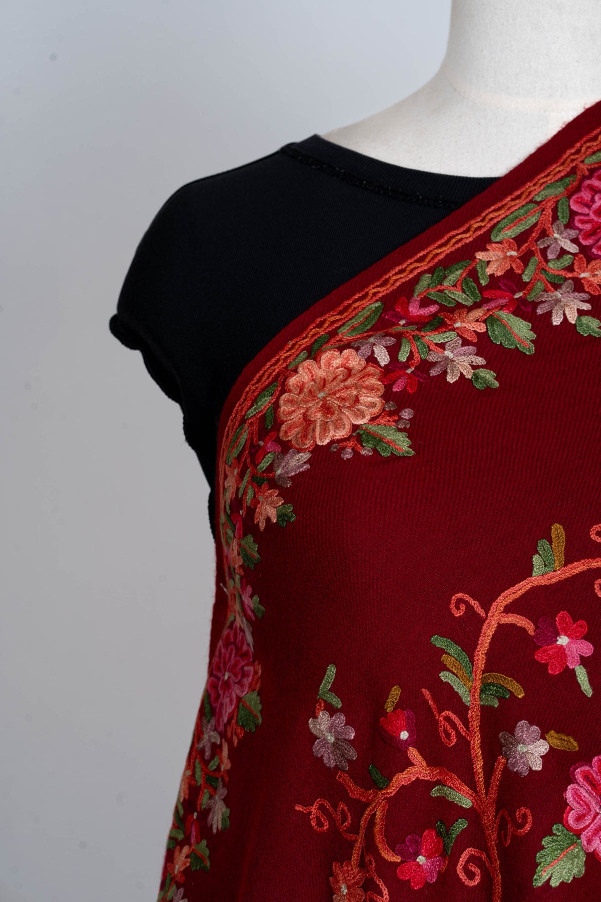 Shoulder detail of a crimson stole with pink and coral Aari flowers, green leaves and a narrow orange-edged floral border