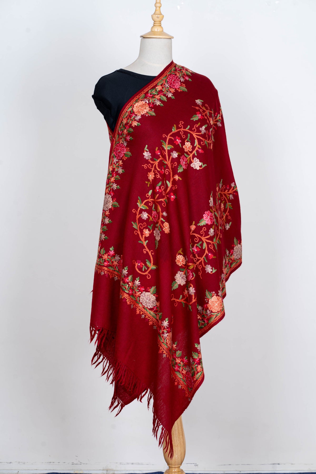 Full drape of a crimson Merino wool stole on a mannequin, with curling Aari floral vines, embroidered borders and fringed ends
