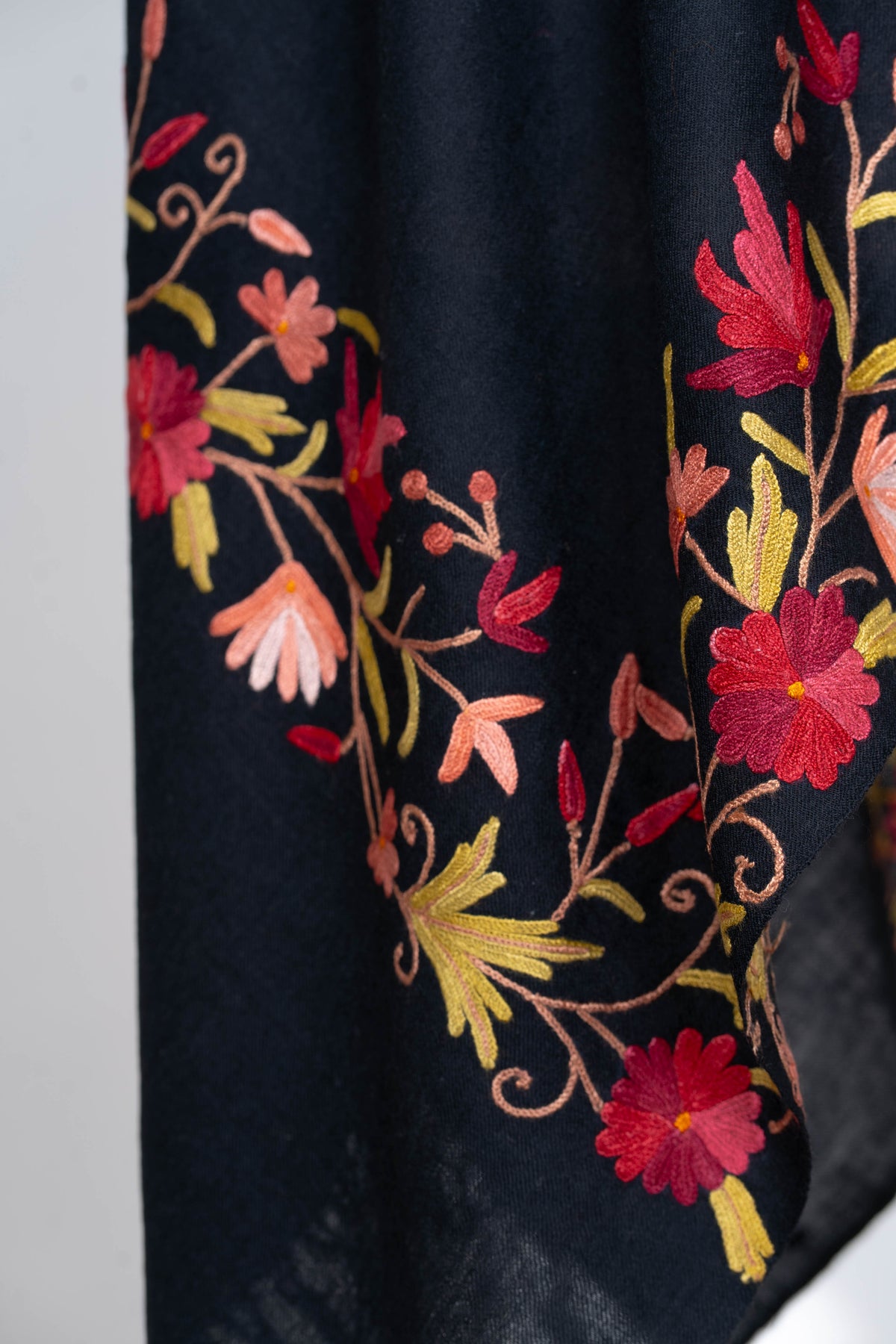 Close-up of red and peach flowers with curling stems and gold-toned leaves along the black stole’s hanging border.