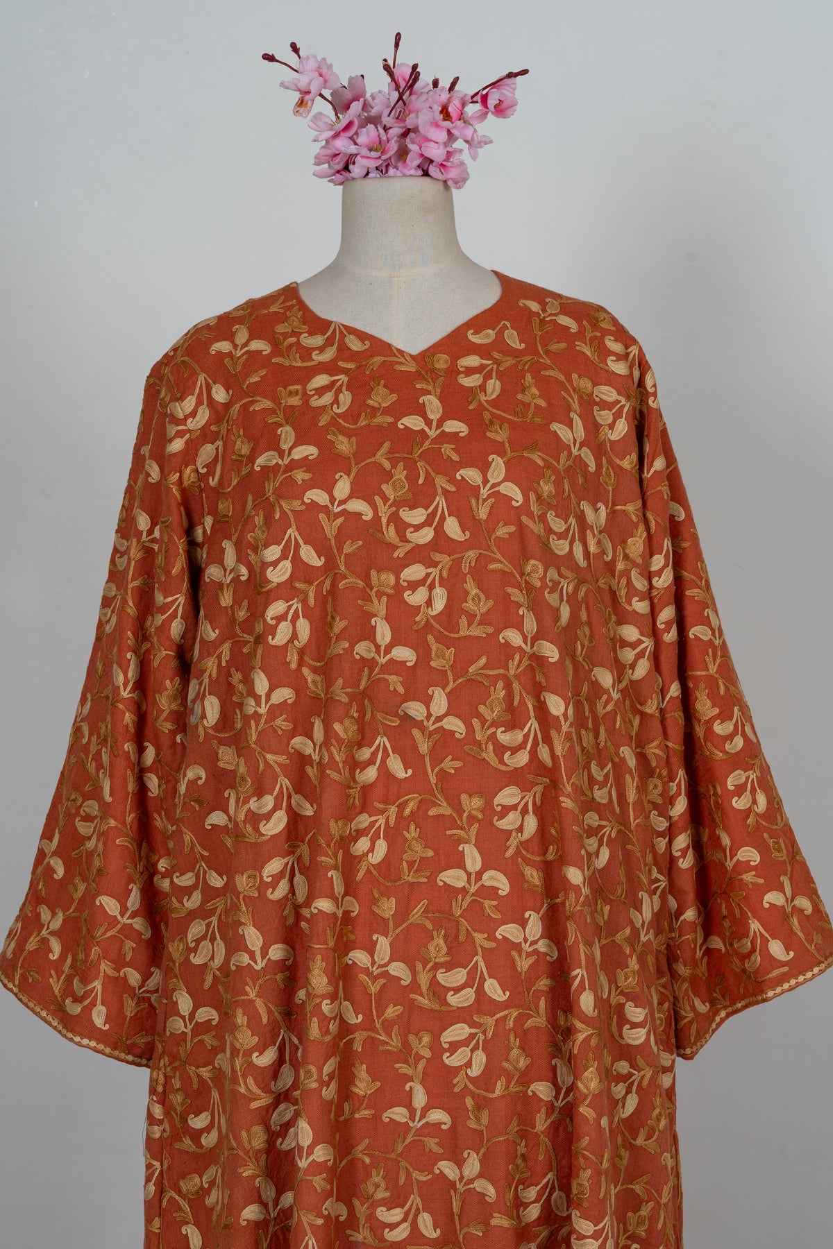 Upper front of a burnt-saffron abaya with a shallow V-neck, wide sleeves and all-over cream and gold Aari vines