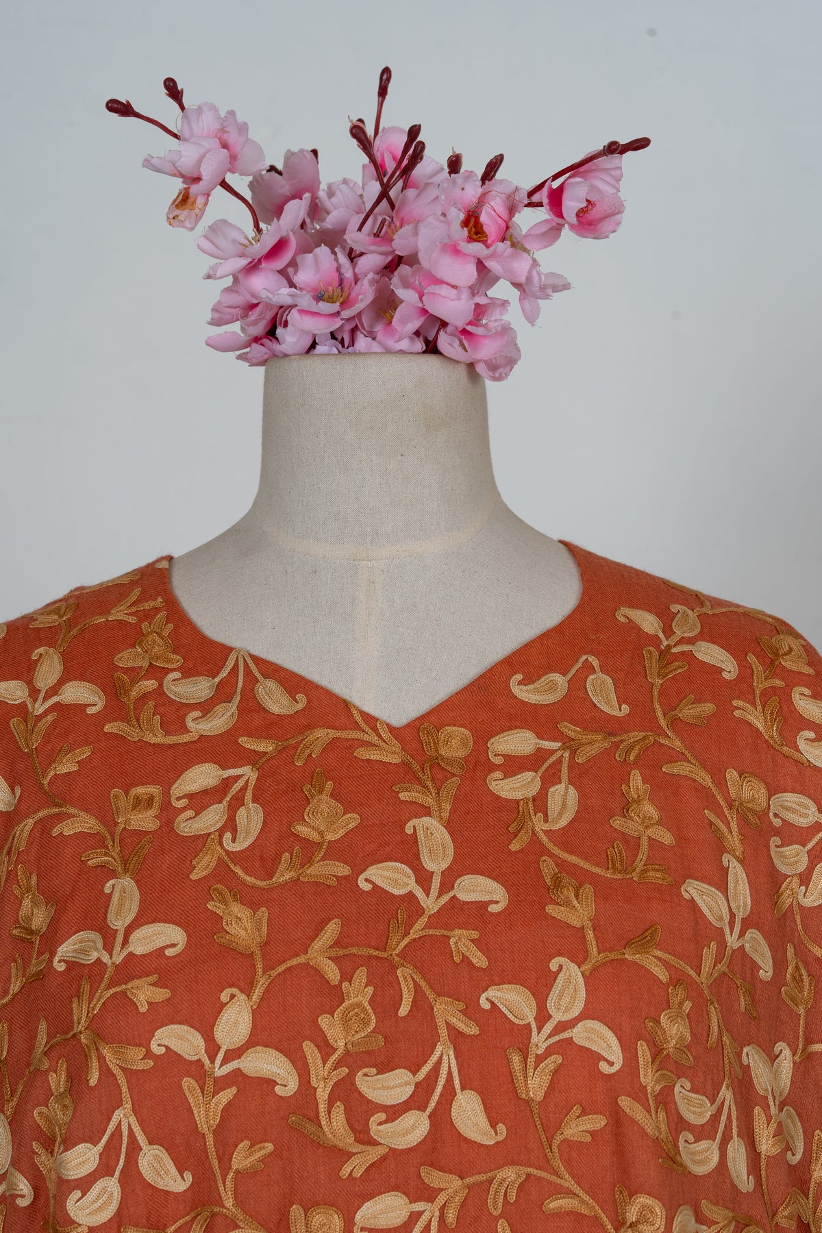 Close-up of a burnt-saffron abaya's shallow V-neck and chest, showing cream and golden Aari leaves and curling stems