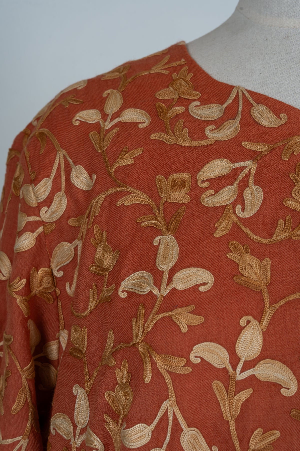 Close-up of cream and gold Aari floral vines across the shoulder of a burnt-saffron abaya
