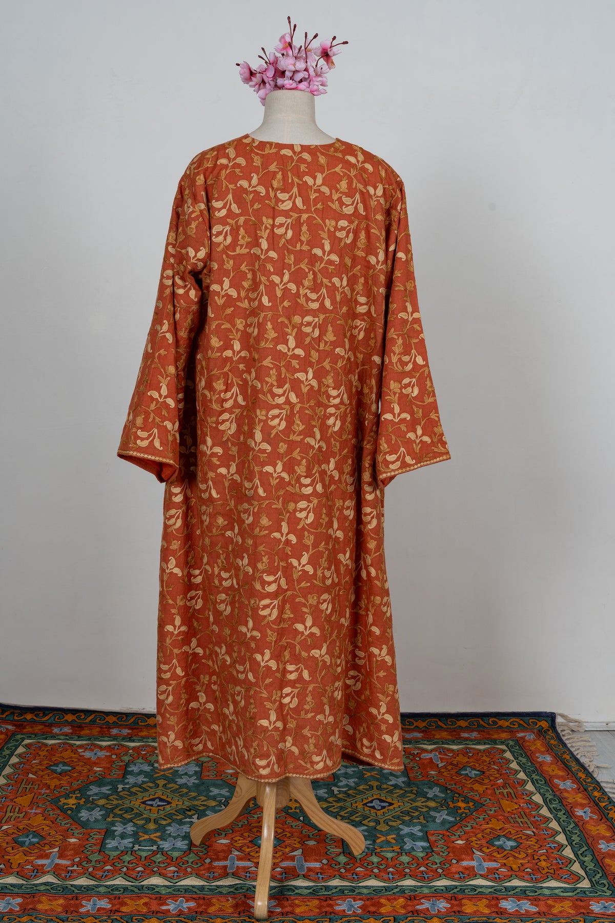 Back of a burnt-saffron abaya on a mannequin, covered in cream and golden Aari floral vines