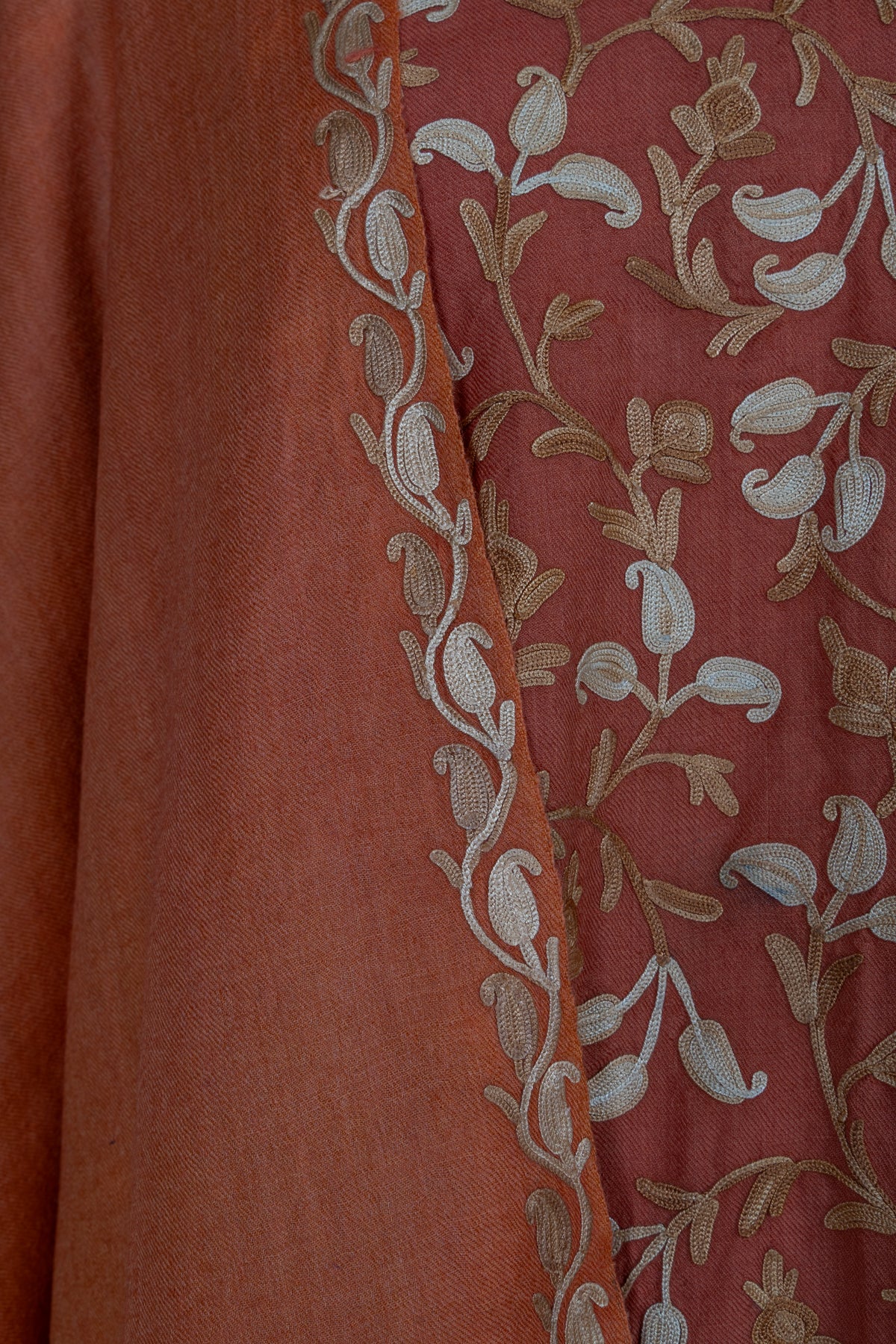 Close-up of a saffron wrap's narrow Aari leaf border beside the matching abaya's cream and gold floral embroidery